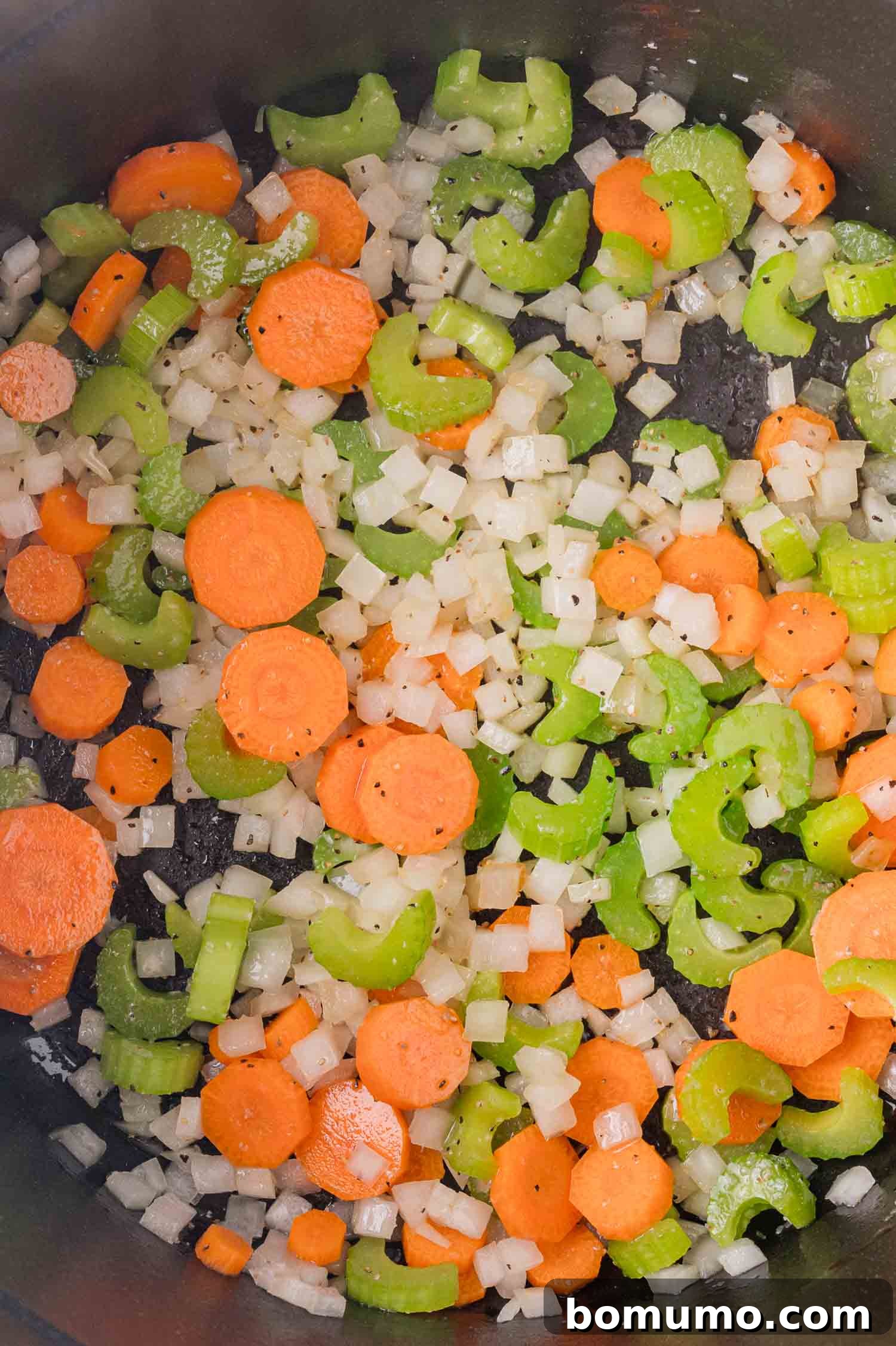 Chopped carrots, celery, and onions sautéing in a pan.