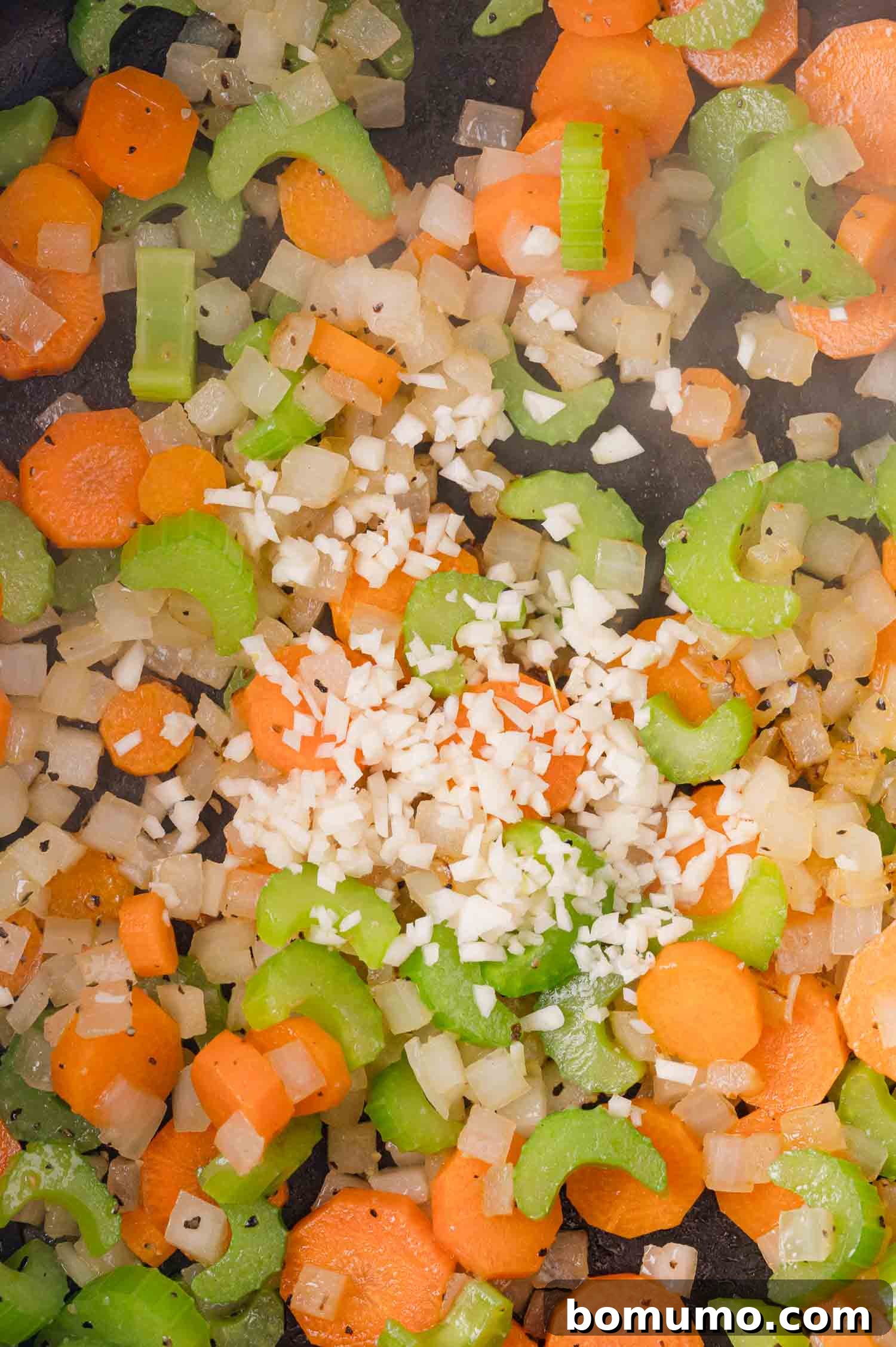 Chopped carrots, celery, onion, and minced garlic sautéing in a pan.