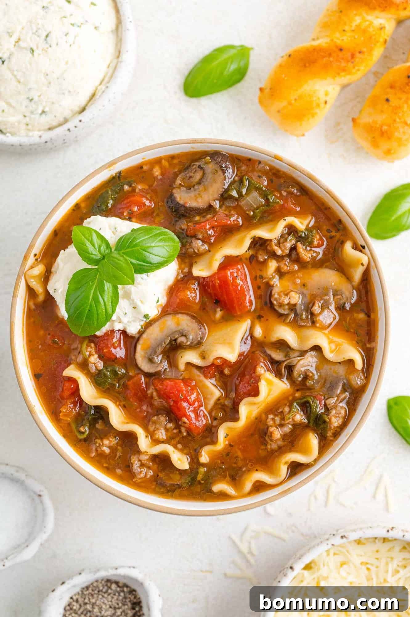 A comforting bowl of lasagna soup, generously topped with melted cheese and fresh basil.