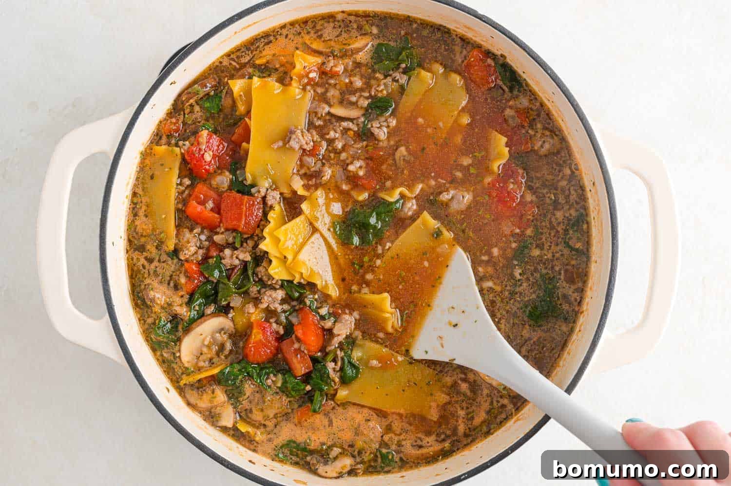 Uncooked lasagna noodles, broken into bite-sized pieces, being added to the simmering soup.