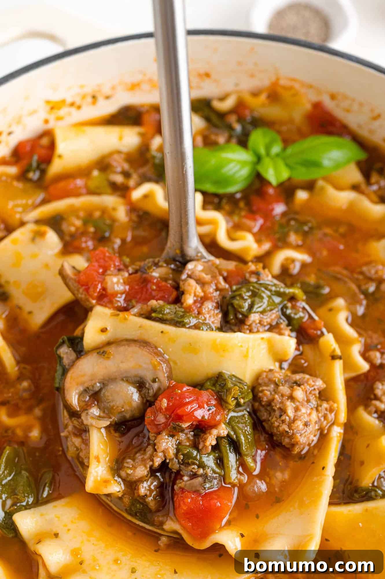 A ladle scooping hot lasagna soup from a large pot, showcasing its rich texture and ingredients.
