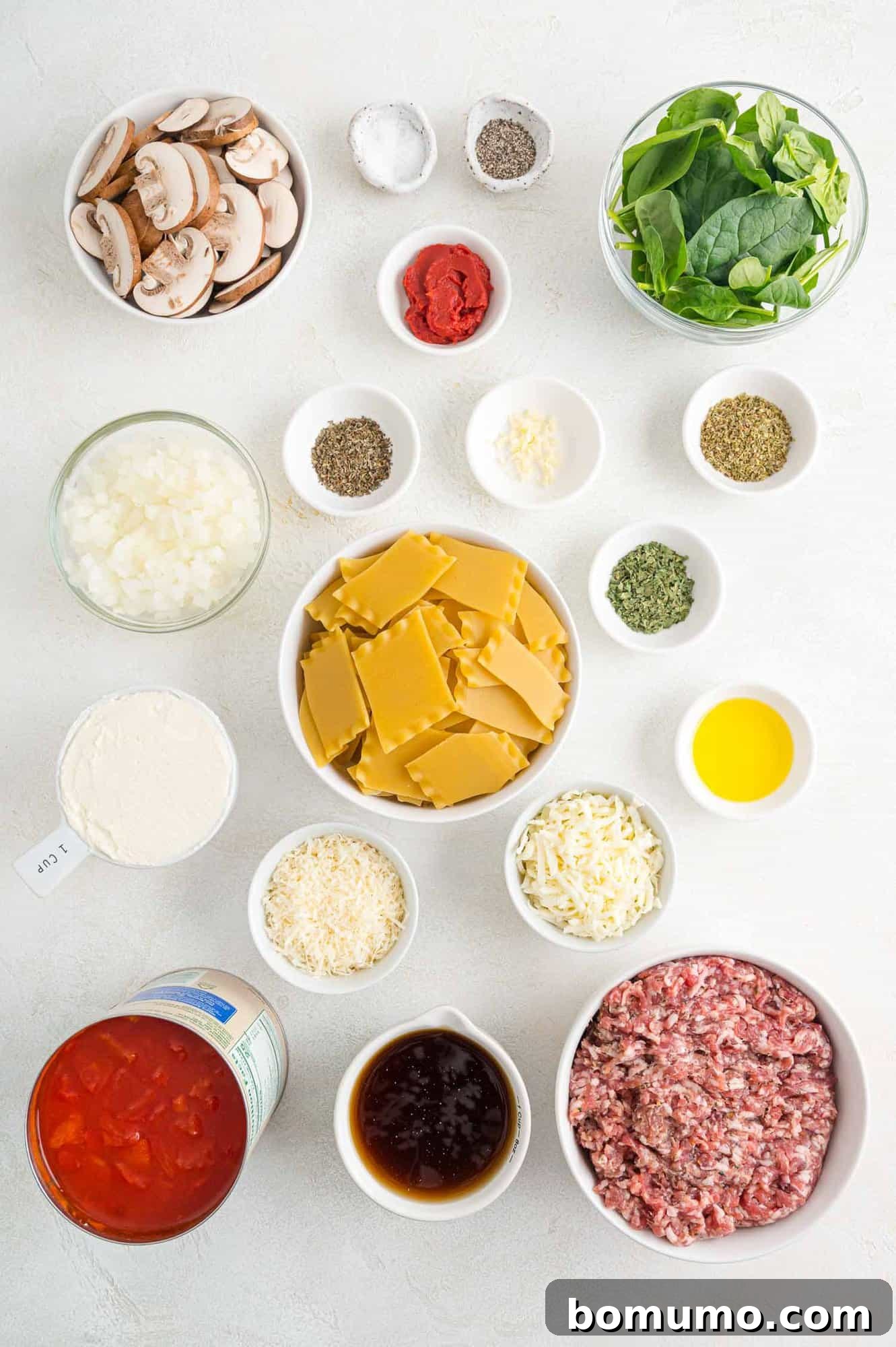 An array of fresh ingredients for lasagna soup, including Italian sausage, diced tomatoes, spinach, mushrooms, and various cheeses, neatly arranged in separate bowls.