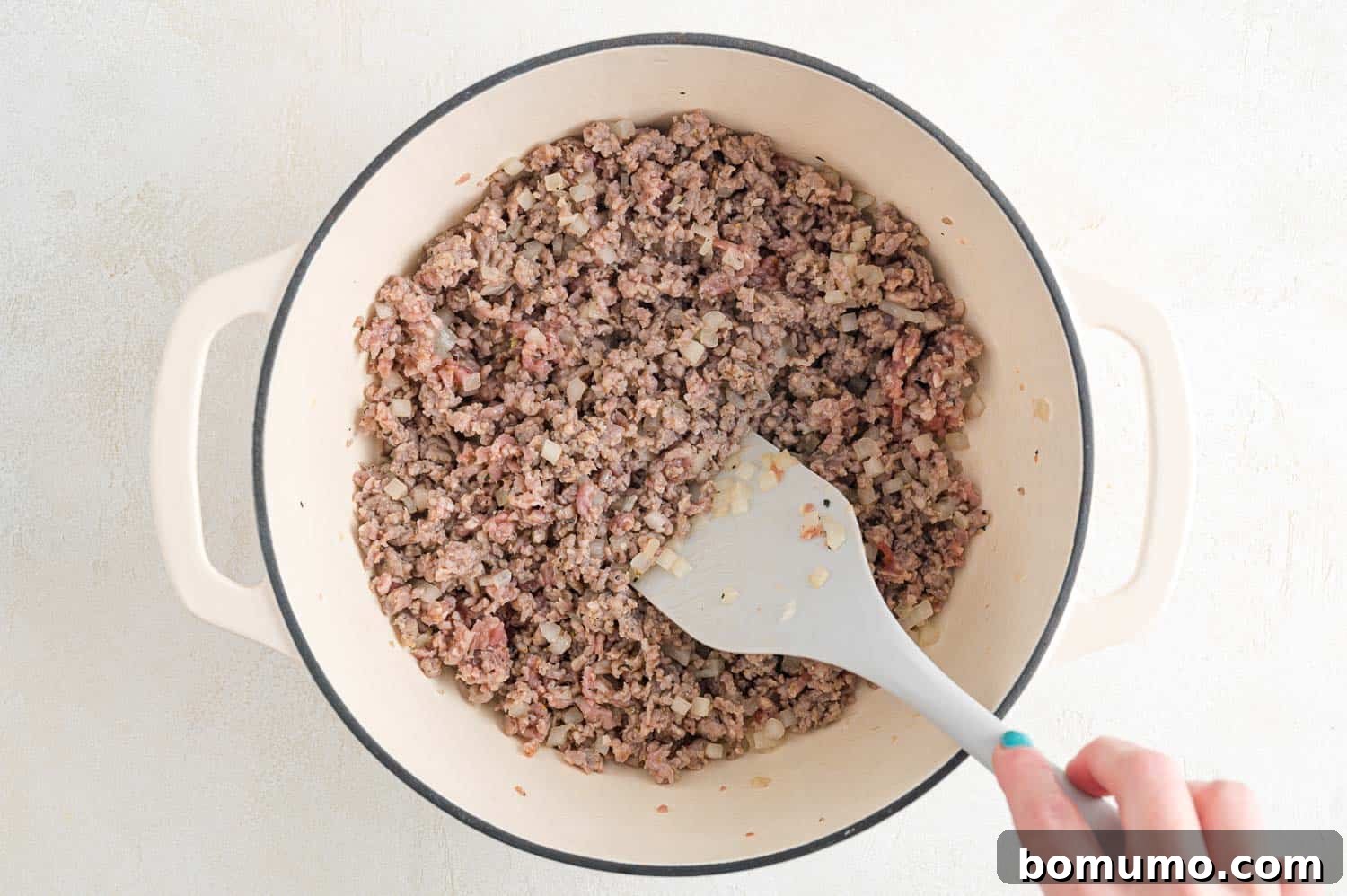 Close-up of Italian sausage and diced onions browning in a large pan.