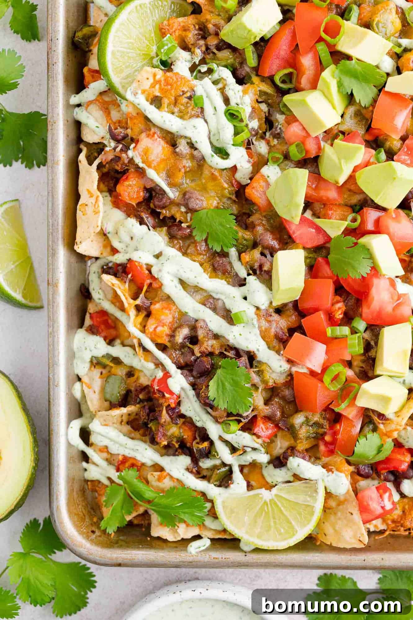 Vegetable nachos on a sheet pan with limes and sour cream drizzle.