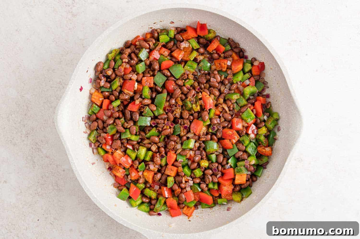 Peppers and onions with black beans and taco seasoning in a frying pan.