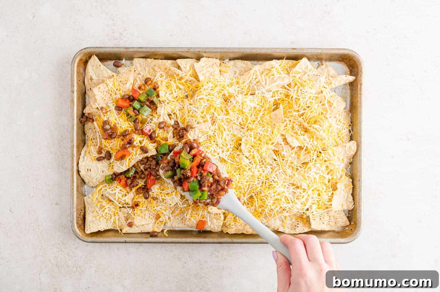 Peppers, onions, and beans being added to nachos.