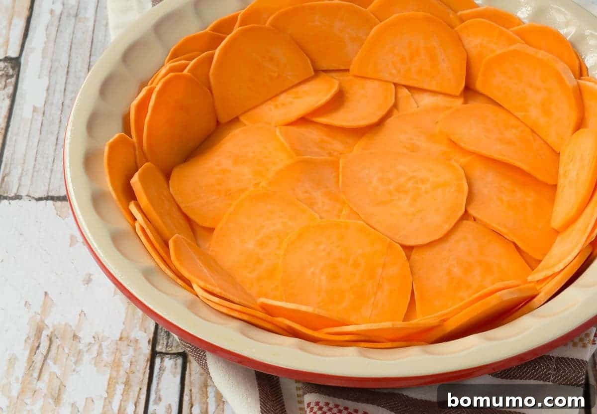 Closeup of thinly sliced sweet potatoes beautifully layered in a pie dish, forming the crust before baking.