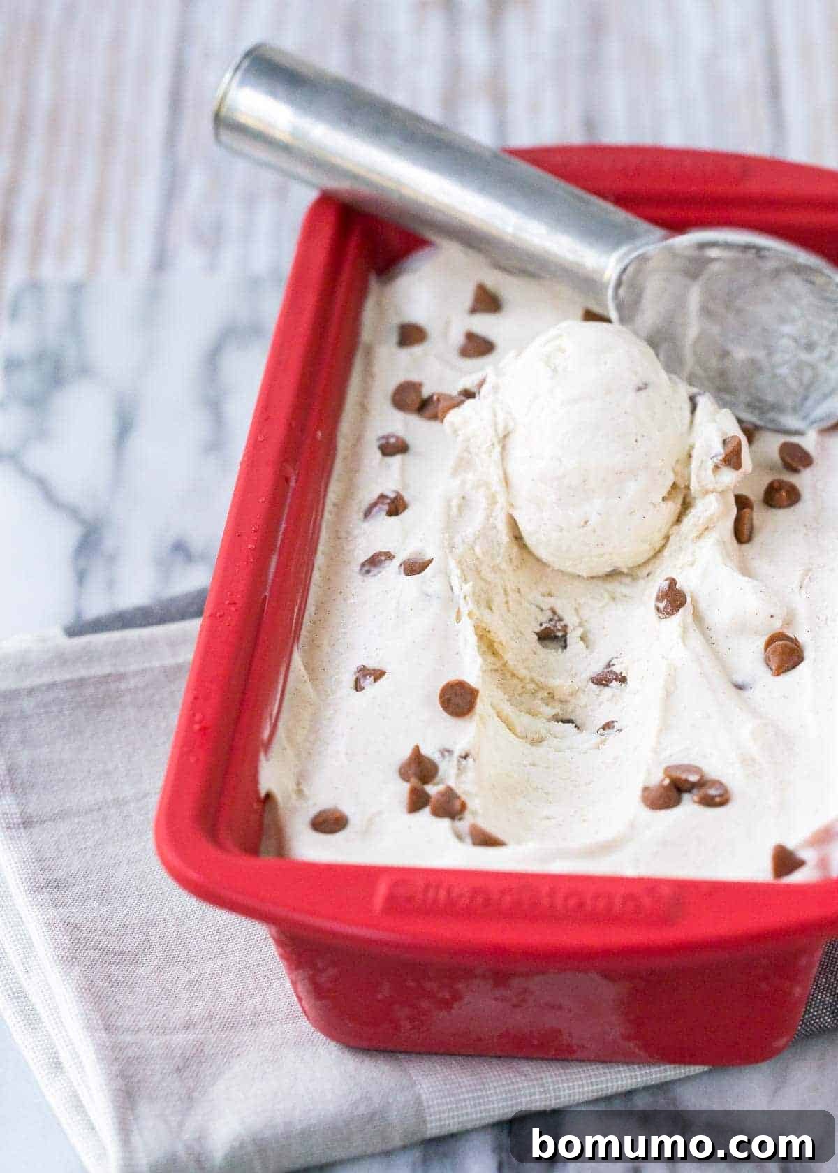 Frozen cinnamon ice cream in a red ceramic loaf pan, with an ice cream scoop.