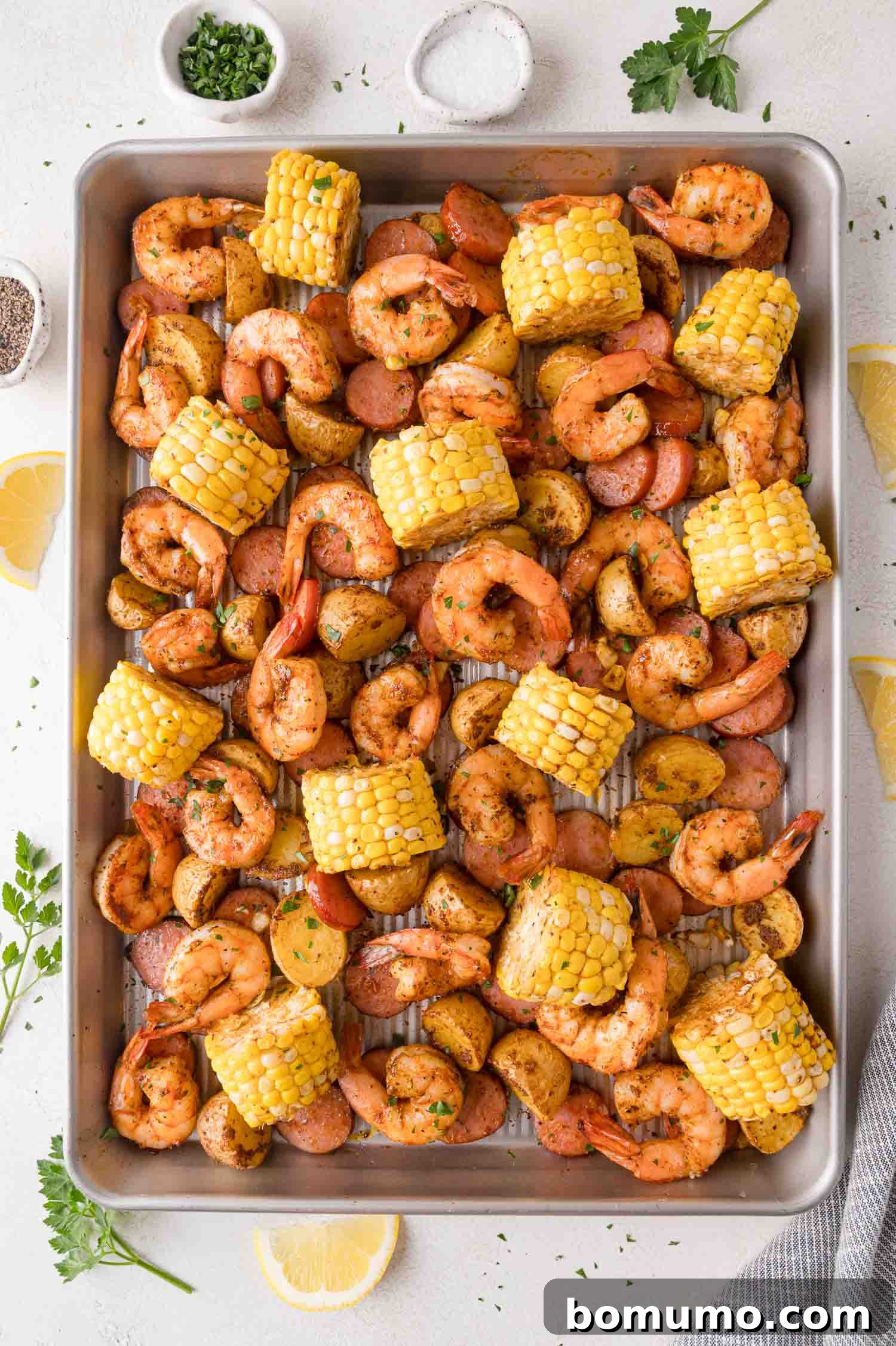 A perfectly cooked sheet pan shrimp boil, featuring seasoned and roasted shrimp, golden-brown sausage slices, vibrant corn on the cob pieces, and tender halved baby potatoes, all garnished with fresh herbs, ready to be served as a complete and delicious meal.