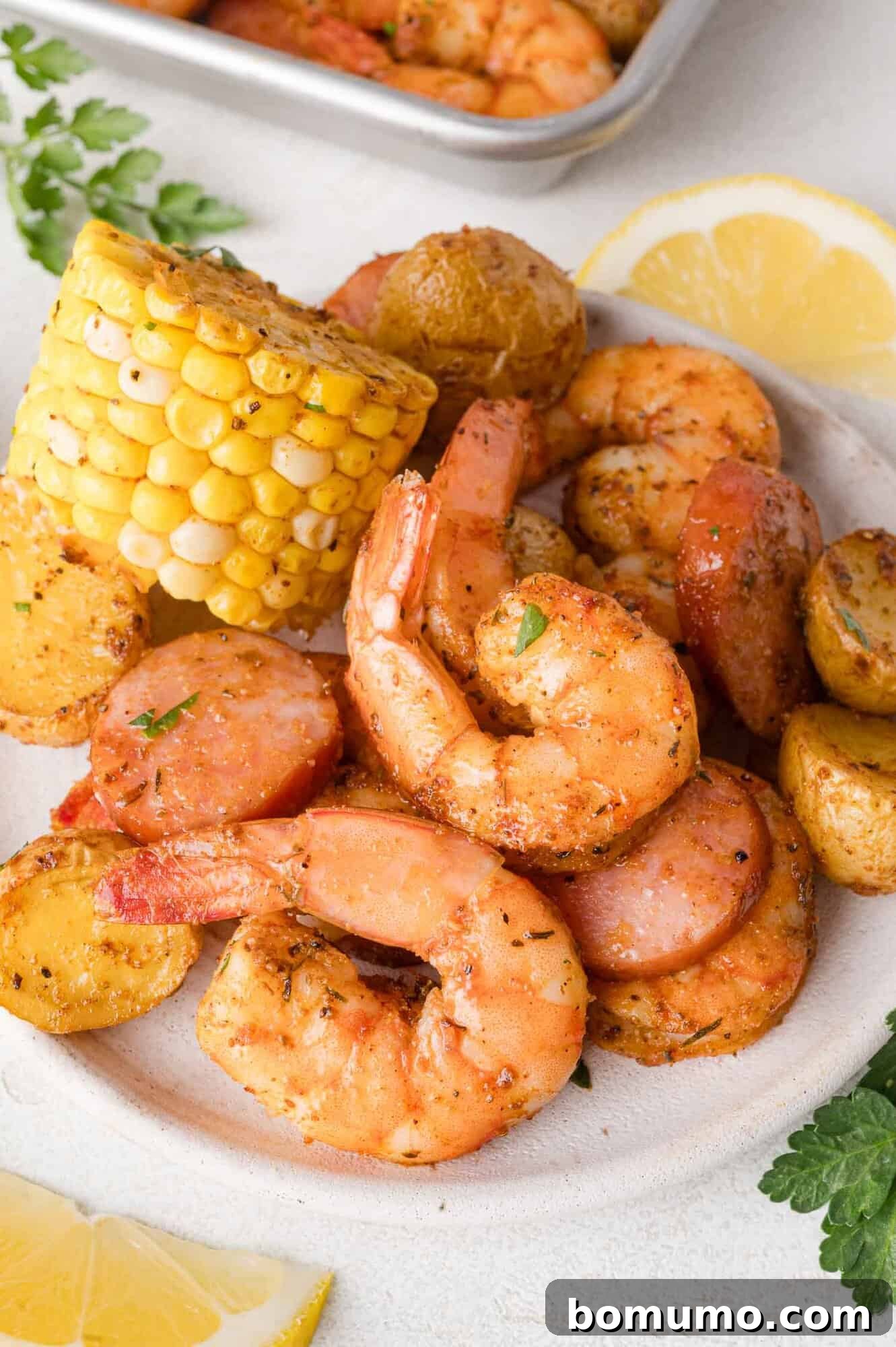 A vibrant individual serving of sheet pan shrimp boil, showcasing succulent cooked shrimp, perfectly roasted sausage slices, tender corn on the cob, and golden seasoned potatoes, all artfully arranged and garnished with fresh parsley and a bright lemon wedge, ready to be enjoyed.