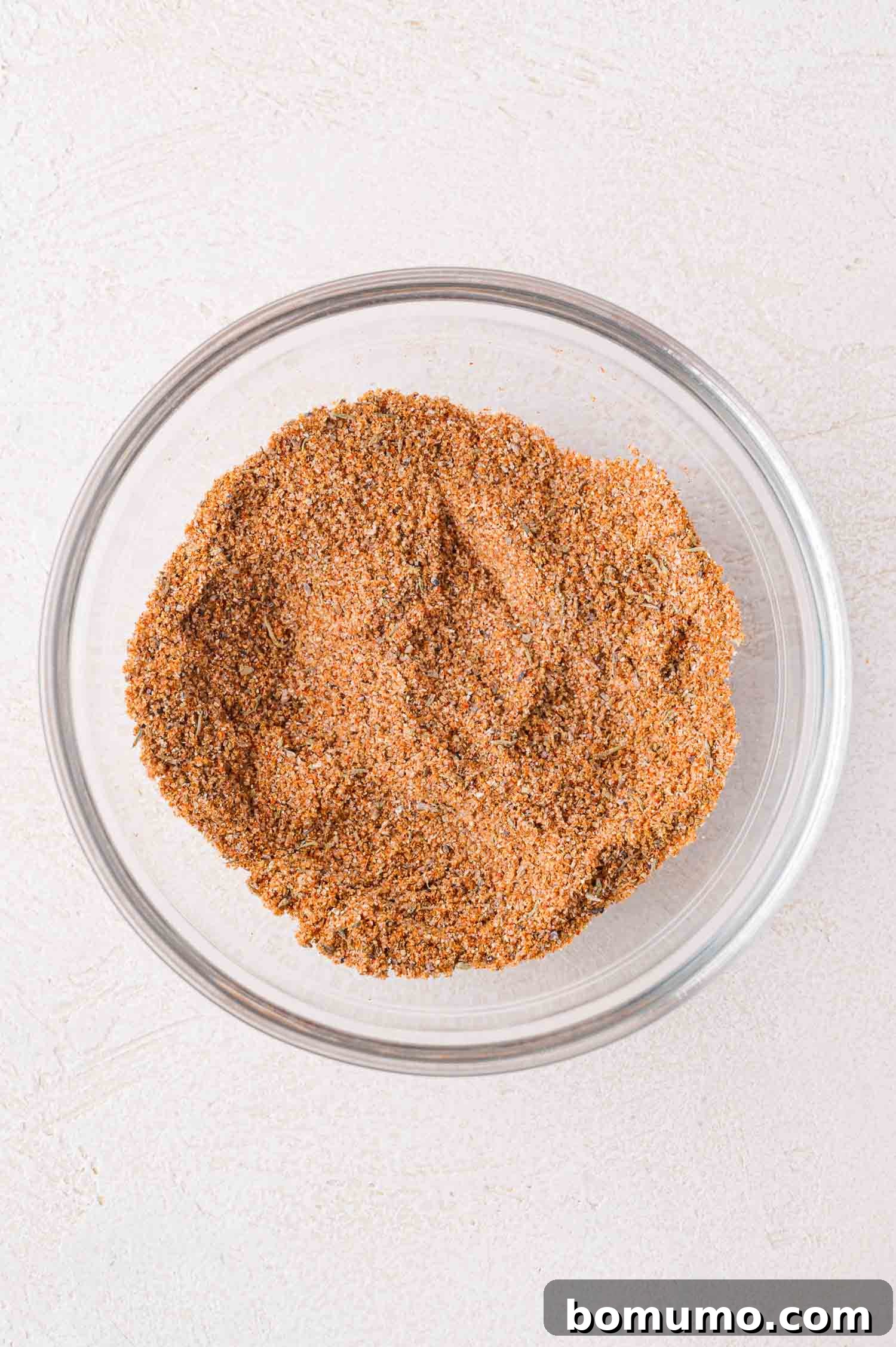 A glass bowl filled with a perfectly mixed blend of dry spices and seasonings for a sheet pan shrimp boil, resting on a light-colored surface.