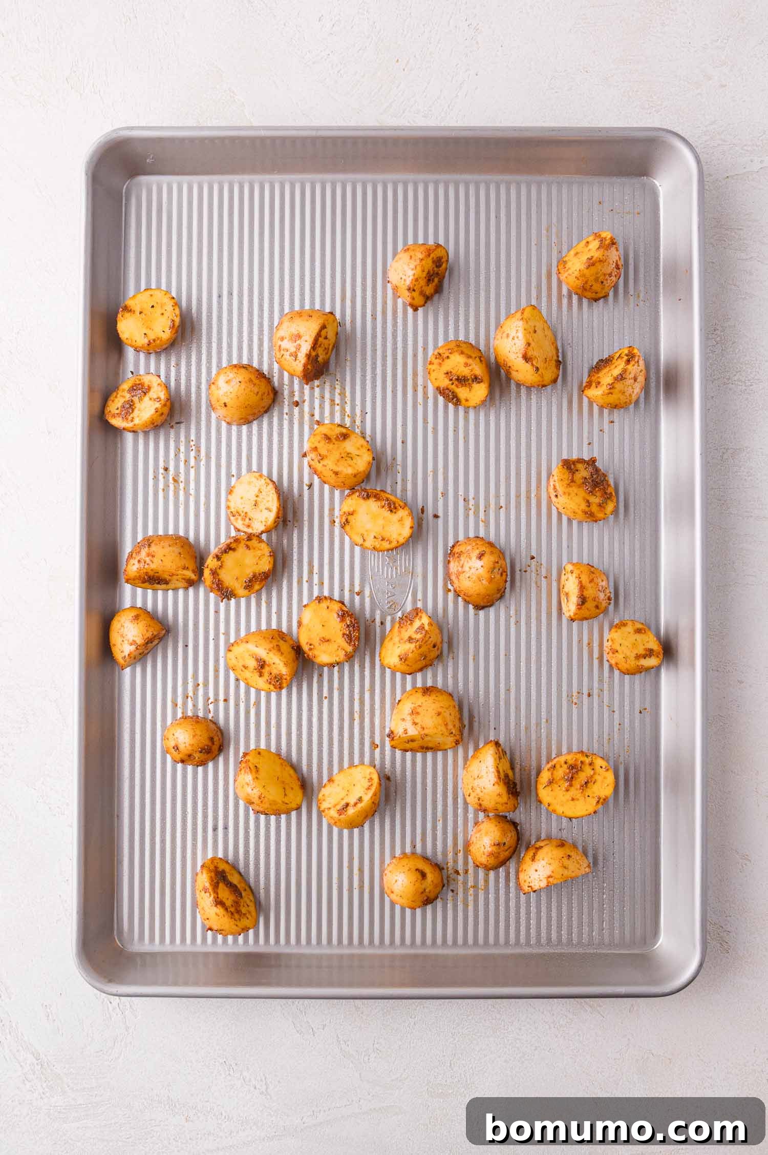 A baking sheet featuring evenly spaced, halved baby potatoes generously seasoned with spices, perfectly arranged and ready for the oven to begin roasting.