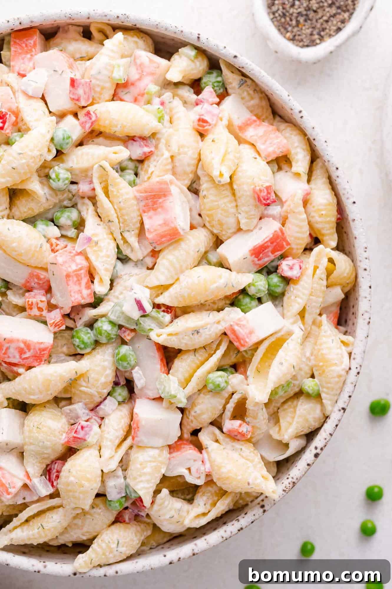 A vibrant bowl of crab pasta salad, showcasing tender pasta shells, green peas, diced imitation crab, and a rich, creamy dressing, ready to be enjoyed.