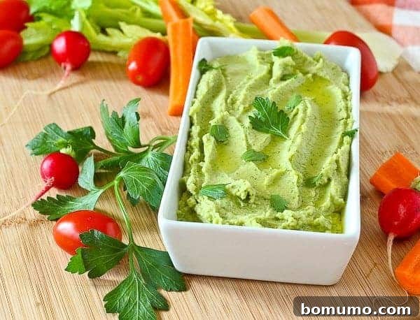 Hummus in serving container, with fresh veggies scattered around.
