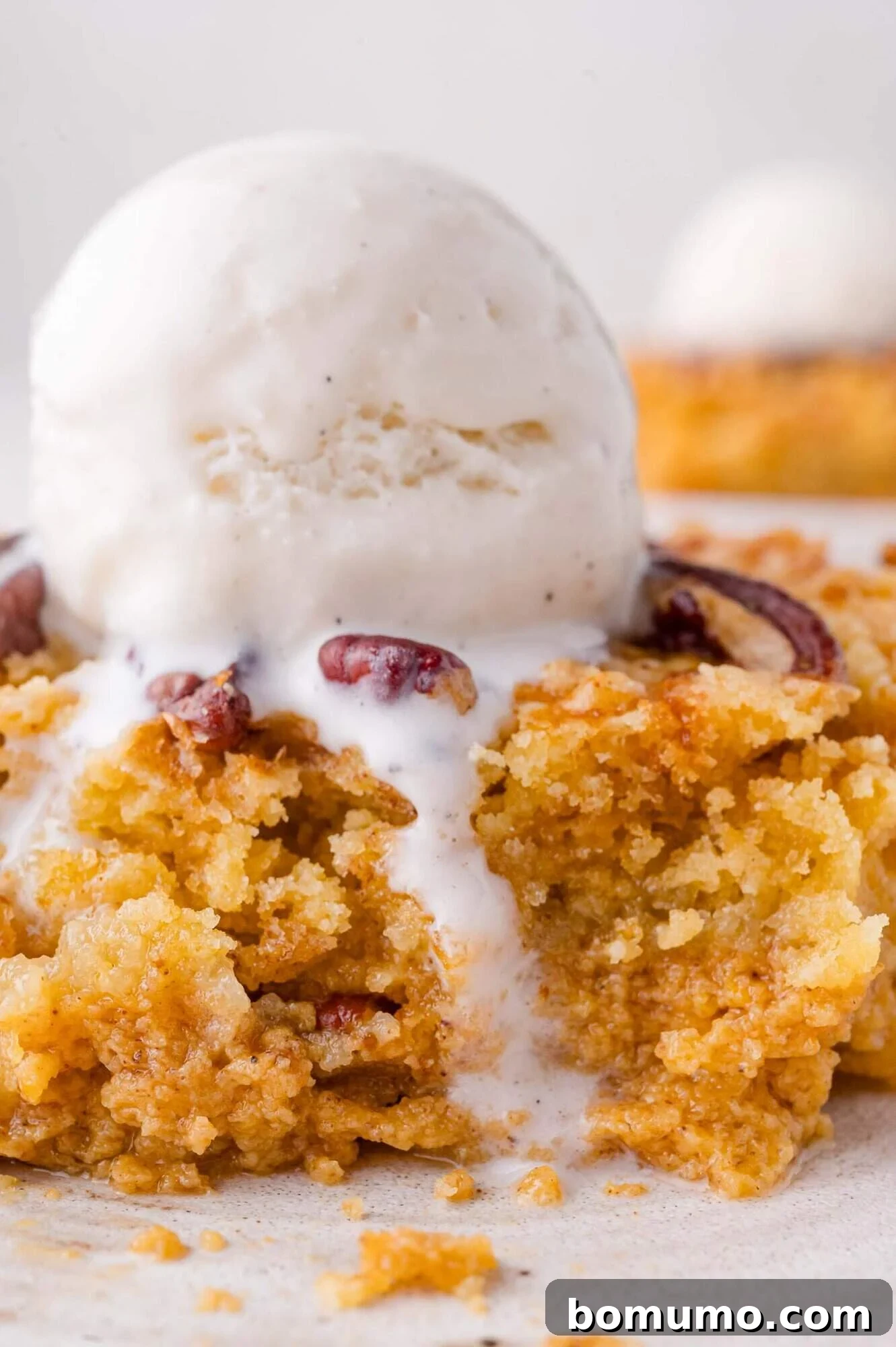 A scoop of vanilla ice cream melting over a serving of crumbly pecan-topped pumpkin dump cake, ready to be enjoyed.
