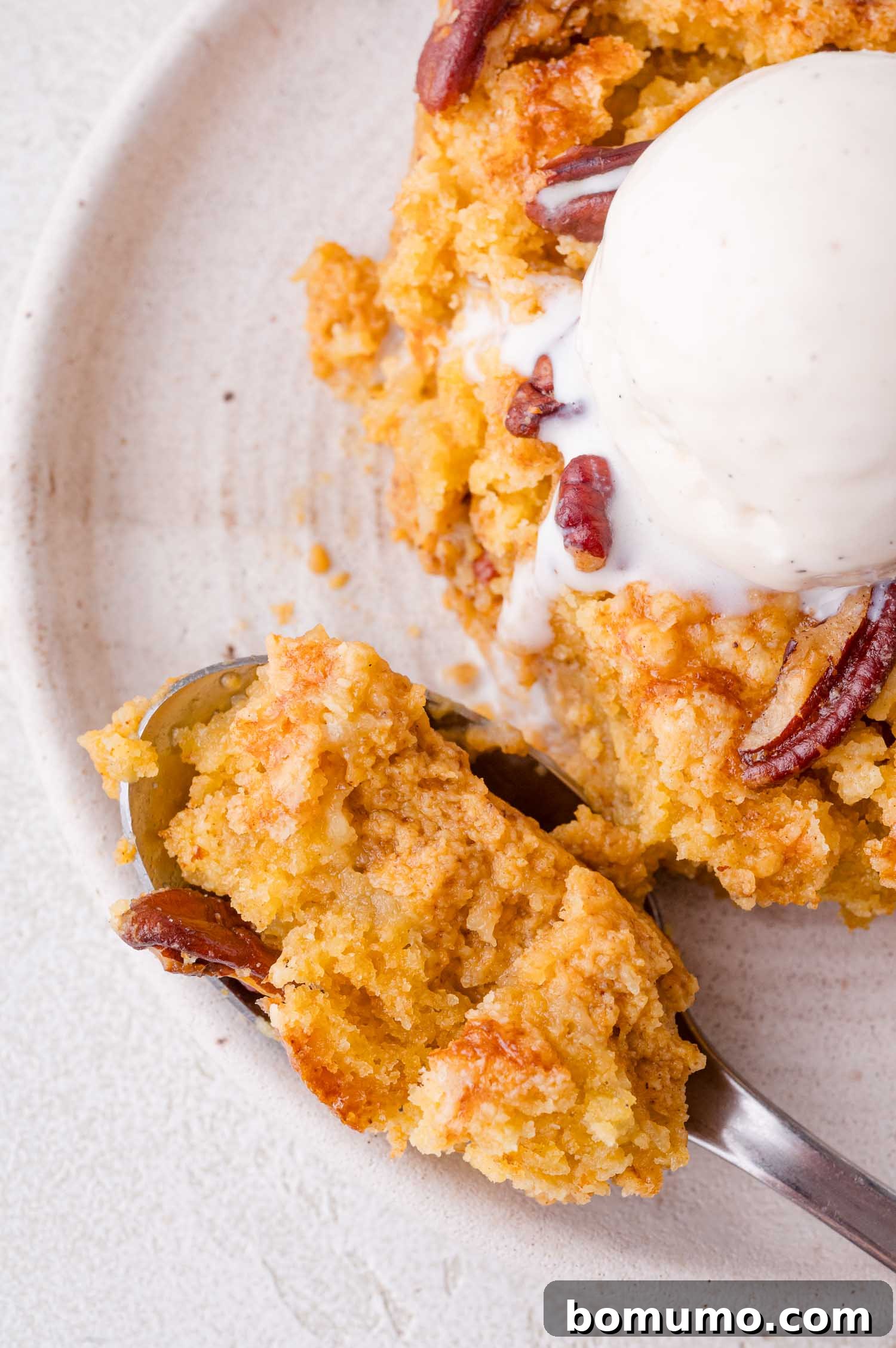 A close-up shot of a spoon scooping into a serving of pumpkin dump cake, perfectly topped with a melting scoop of vanilla ice cream, presented on a plate to highlight its enticing textures.