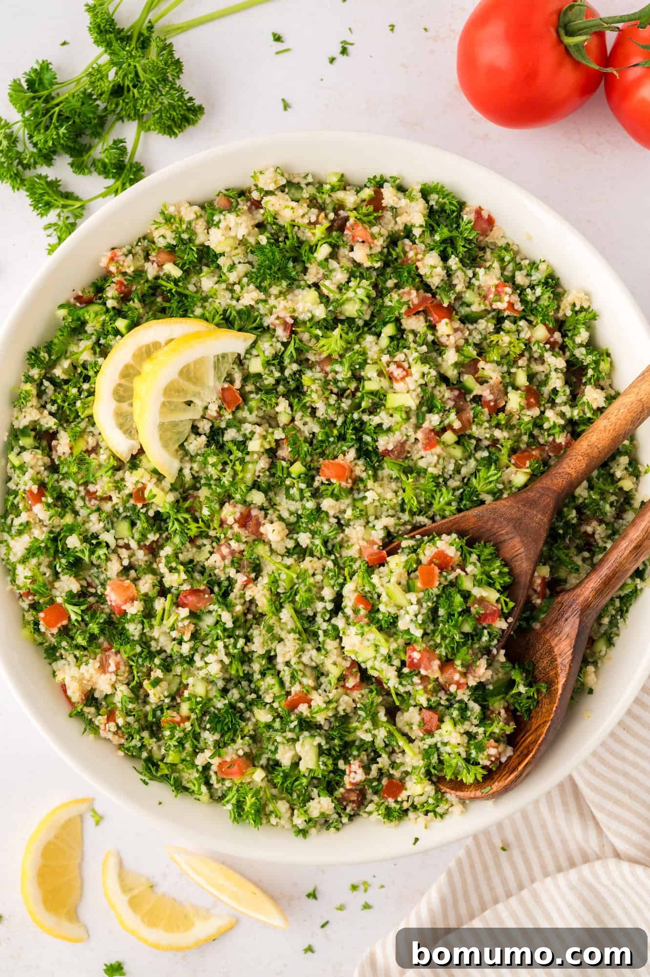 A large bowl filled with vibrant tabbouleh salad, accompanied by two elegant wooden serving spoons.