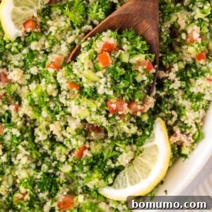 Tabbouleh salad with a large wooden spoon, garnished with lemon slices, ready to be served.