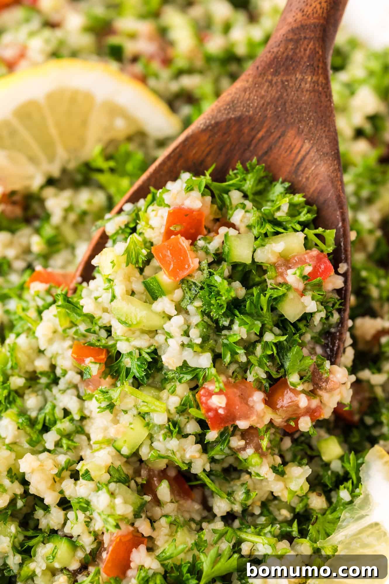 A close-up view of a serving of tabbouleh salad resting on a large wooden serving spoon, highlighting the finely chopped herbs and vegetables.