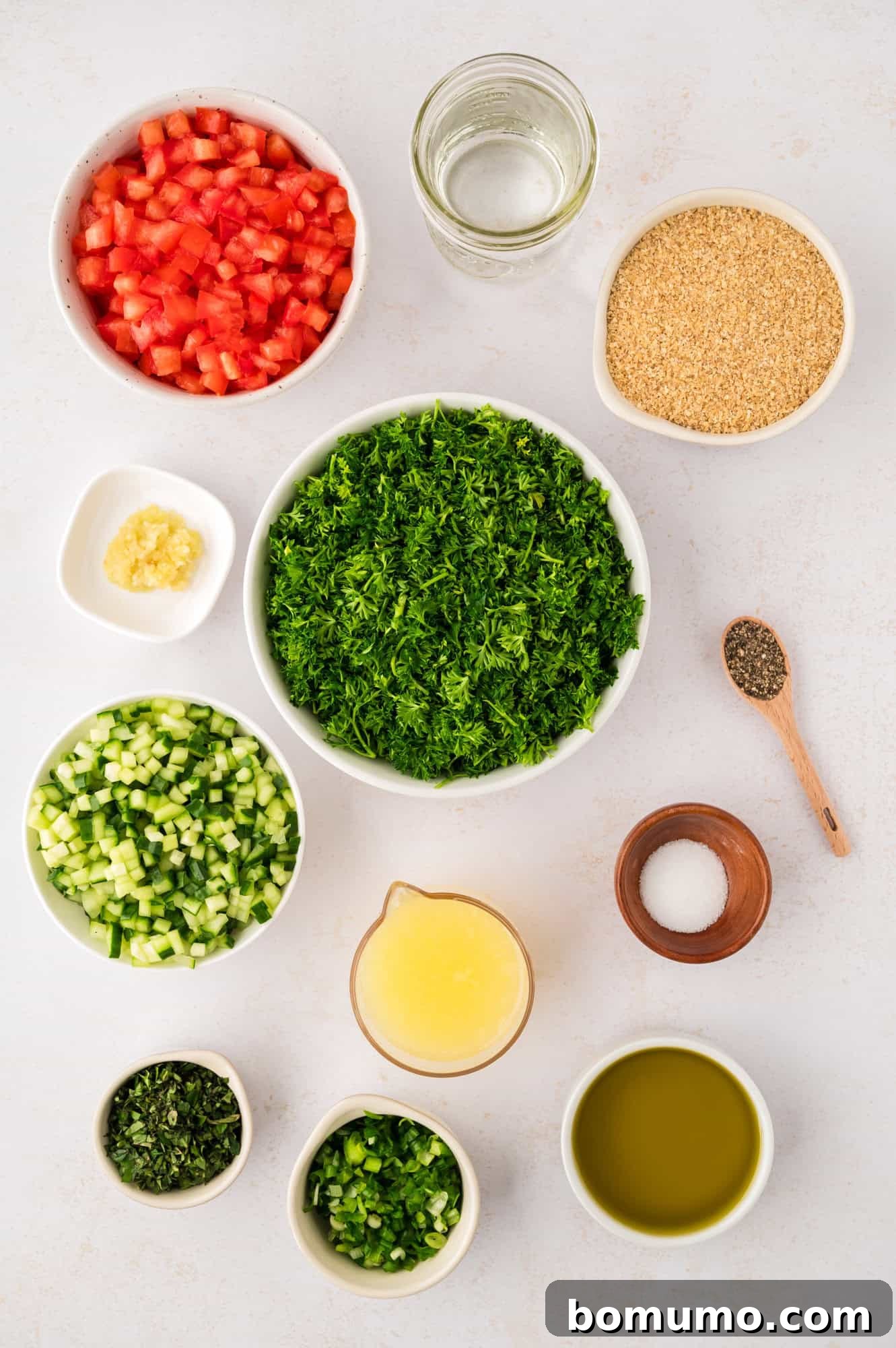 An overhead shot showcasing an array of fresh ingredients meticulously arranged, ready for crafting tabbouleh salad. Highlighted are bunches of vibrant parsley and mint, plump tomatoes, crisp cucumbers, and golden bulgur wheat.