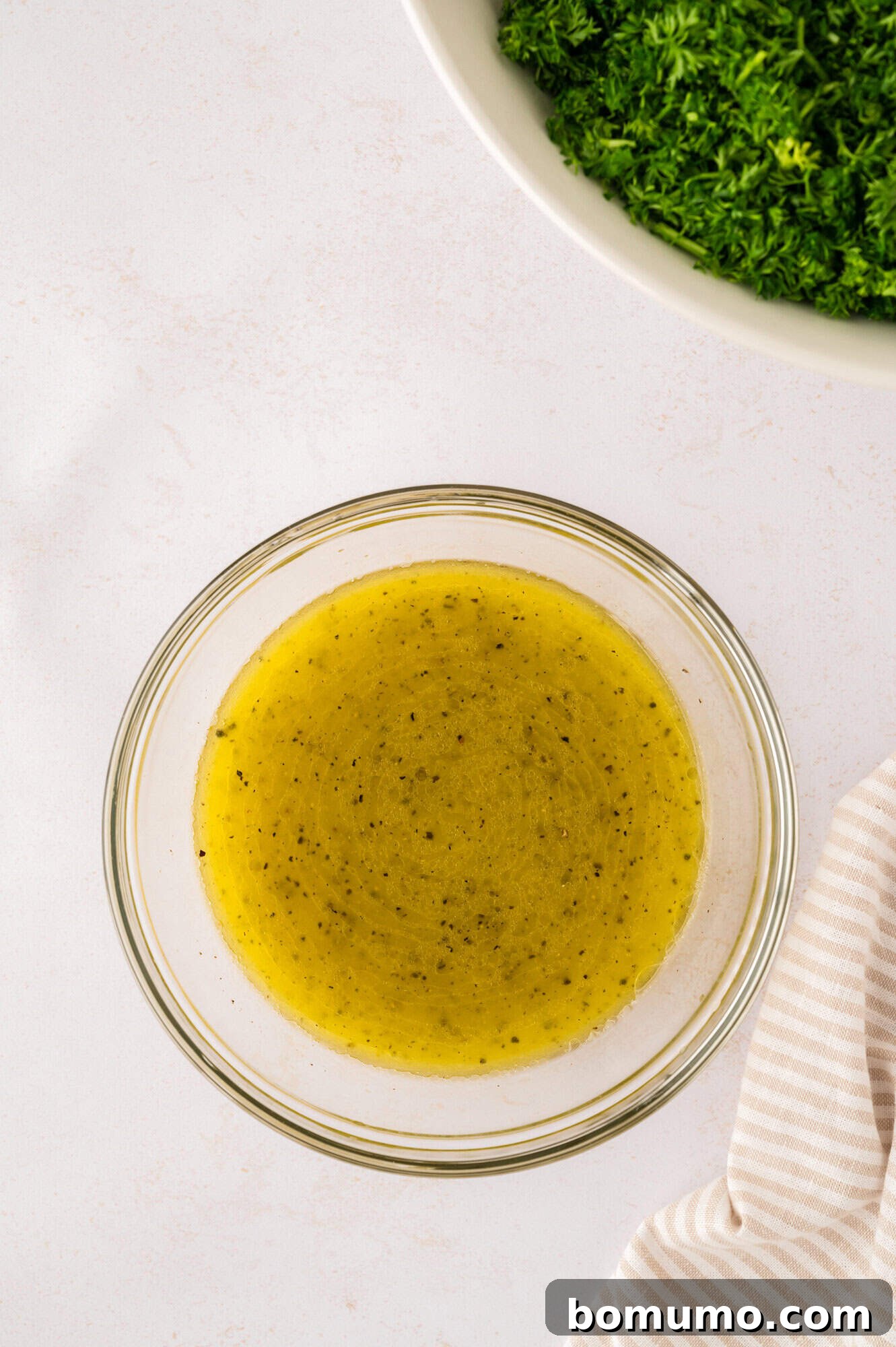 A small, clear glass bowl holding the vibrant and zesty tabbouleh dressing.