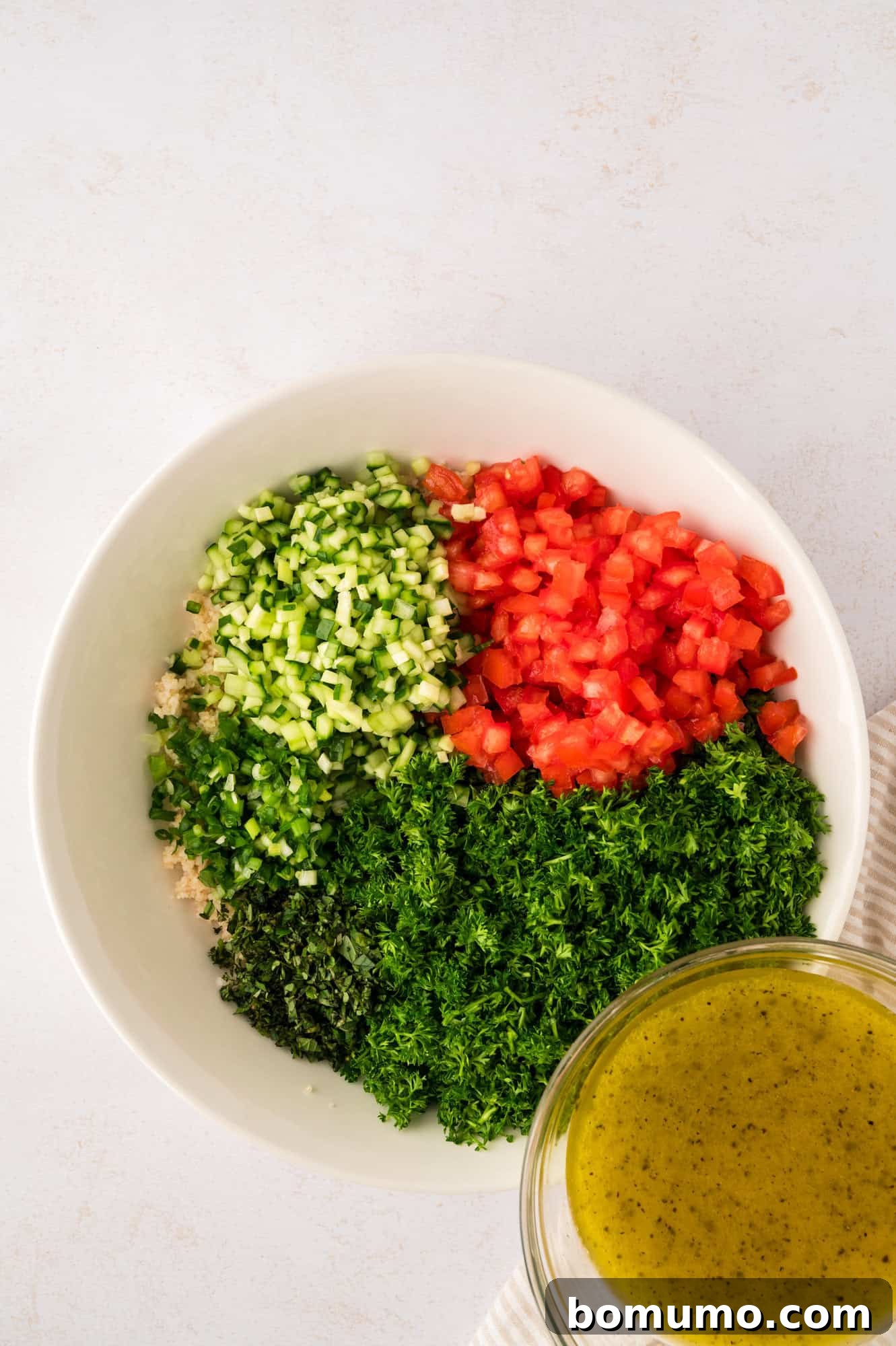 The zesty dressing being poured generously over the fresh tabbouleh ingredients in a large bowl.
