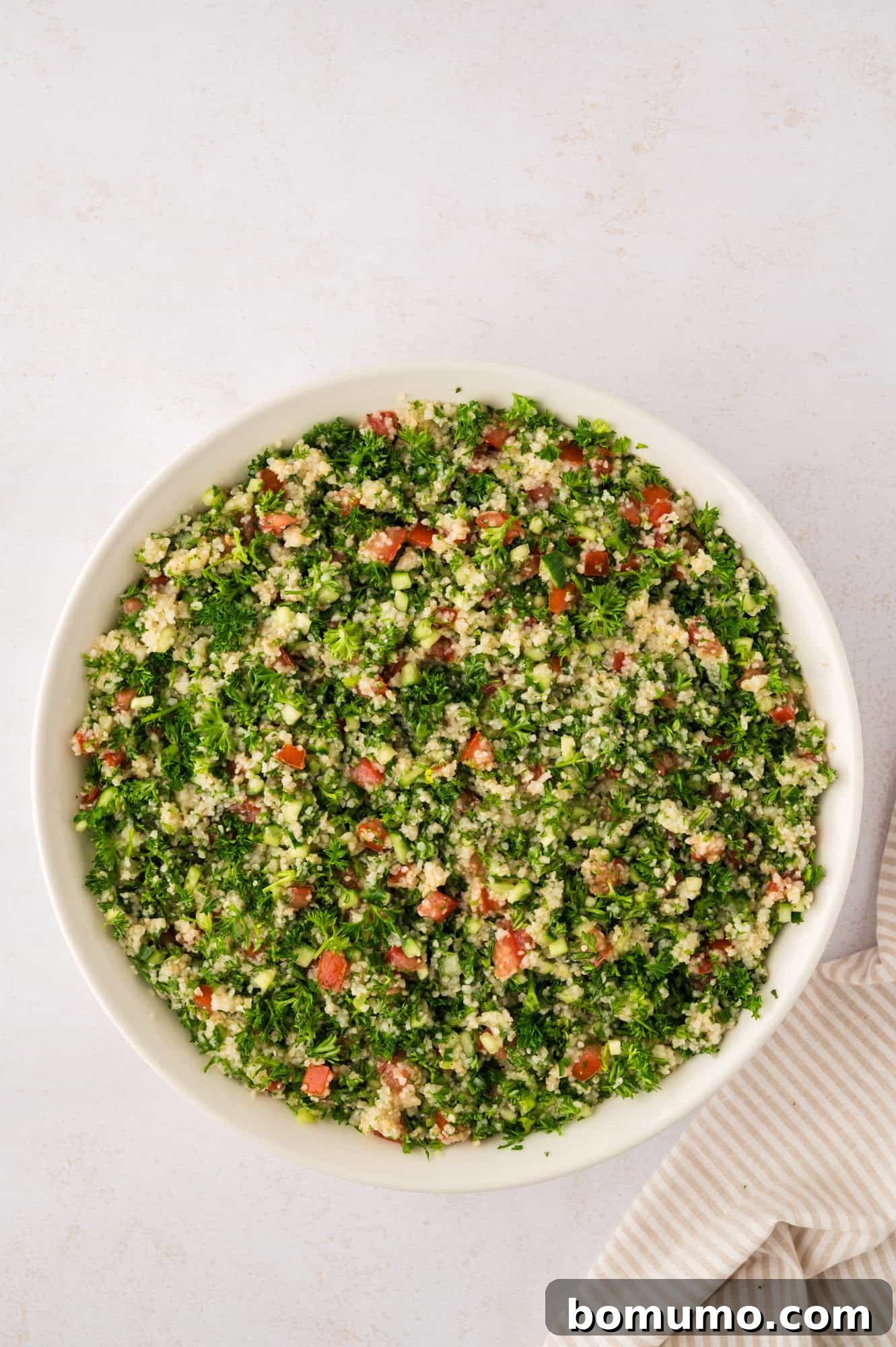 A large white bowl brimming with perfectly mixed tabbouleh salad, vibrant and ready for chilling.