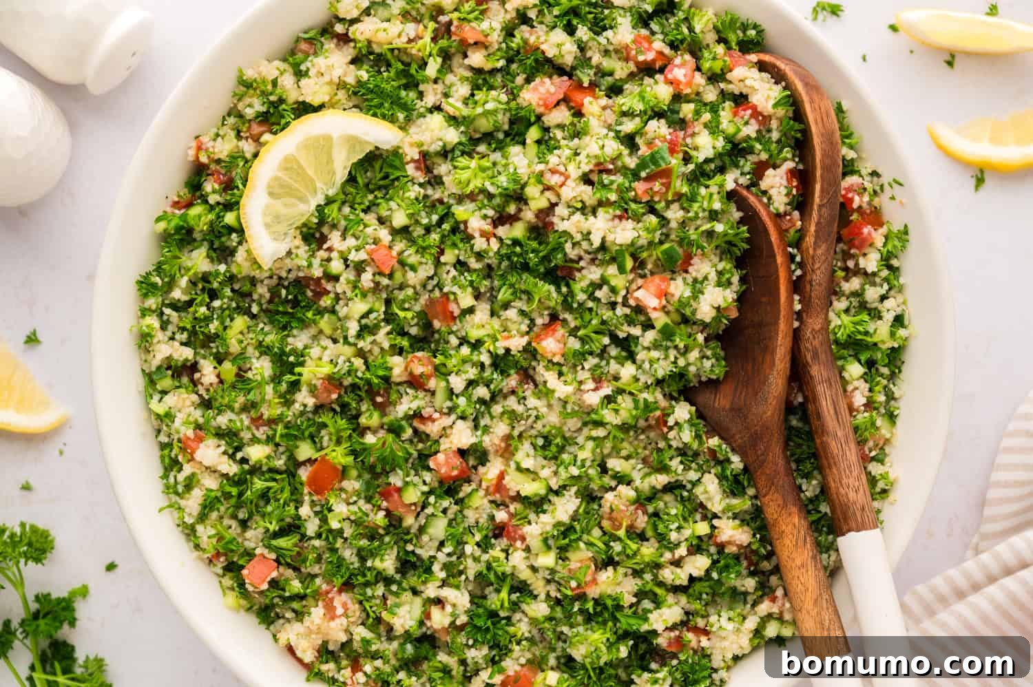 A beautifully presented tabbouleh salad in a large serving bowl, garnished with fresh lemon slices and accompanied by elegant serving utensils.