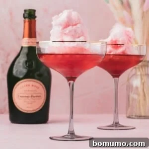 Two cocktail glasses filled with pink cotton candy and a pink liquid, placed next to a bottle of Laurent-Perrier champagne on a pink surface.