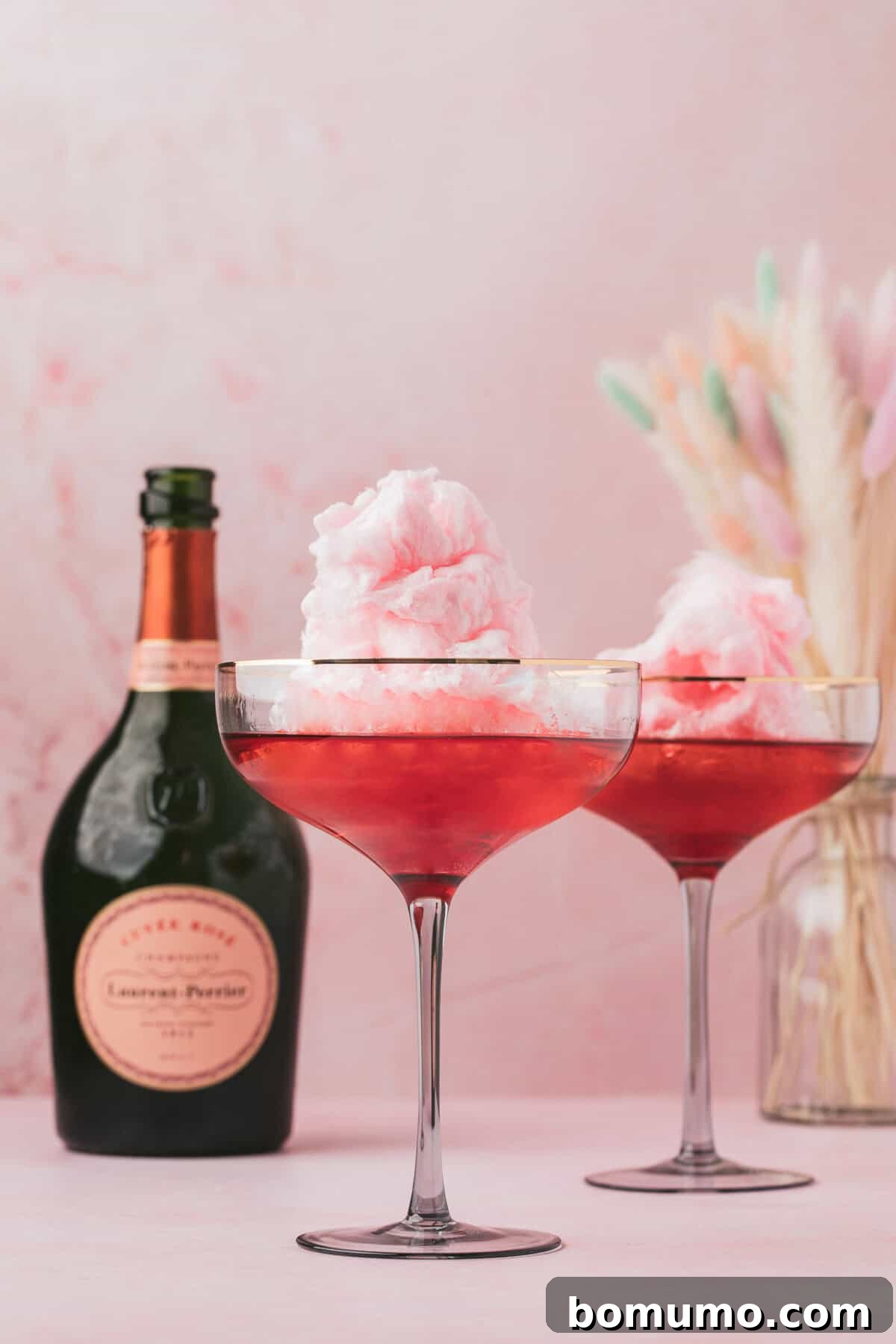 Two elegantly presented pink cotton candy cocktails, each topped with a cloud of cotton candy, resting on a stylish pink surface.