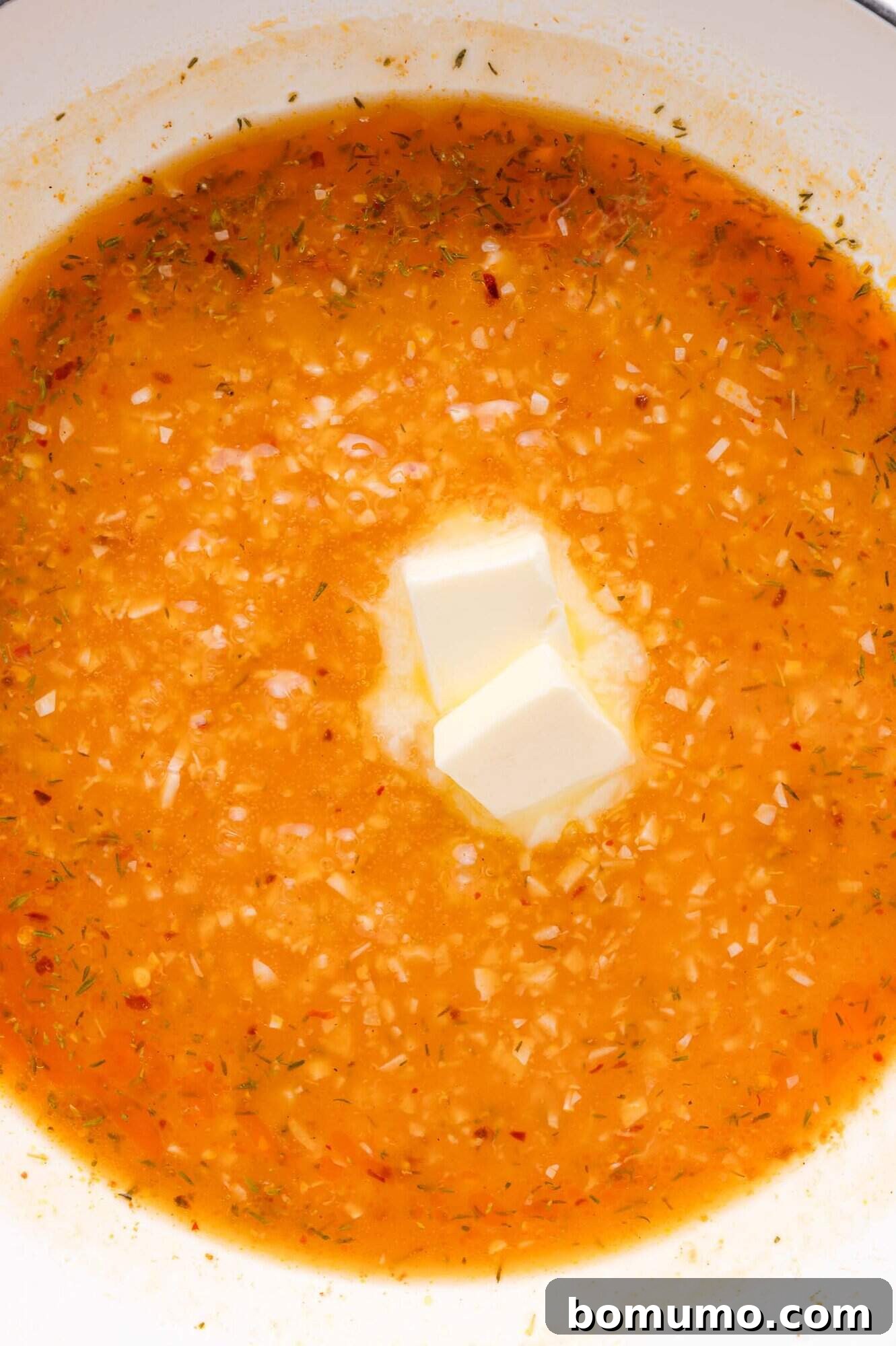 Finely diced garlic and a medley of aromatic spices are gently simmering in a pot, with two golden cubes of butter melting gracefully in the center, gradually enriching the burgeoning sauce for the Lemon Butter Chicken.