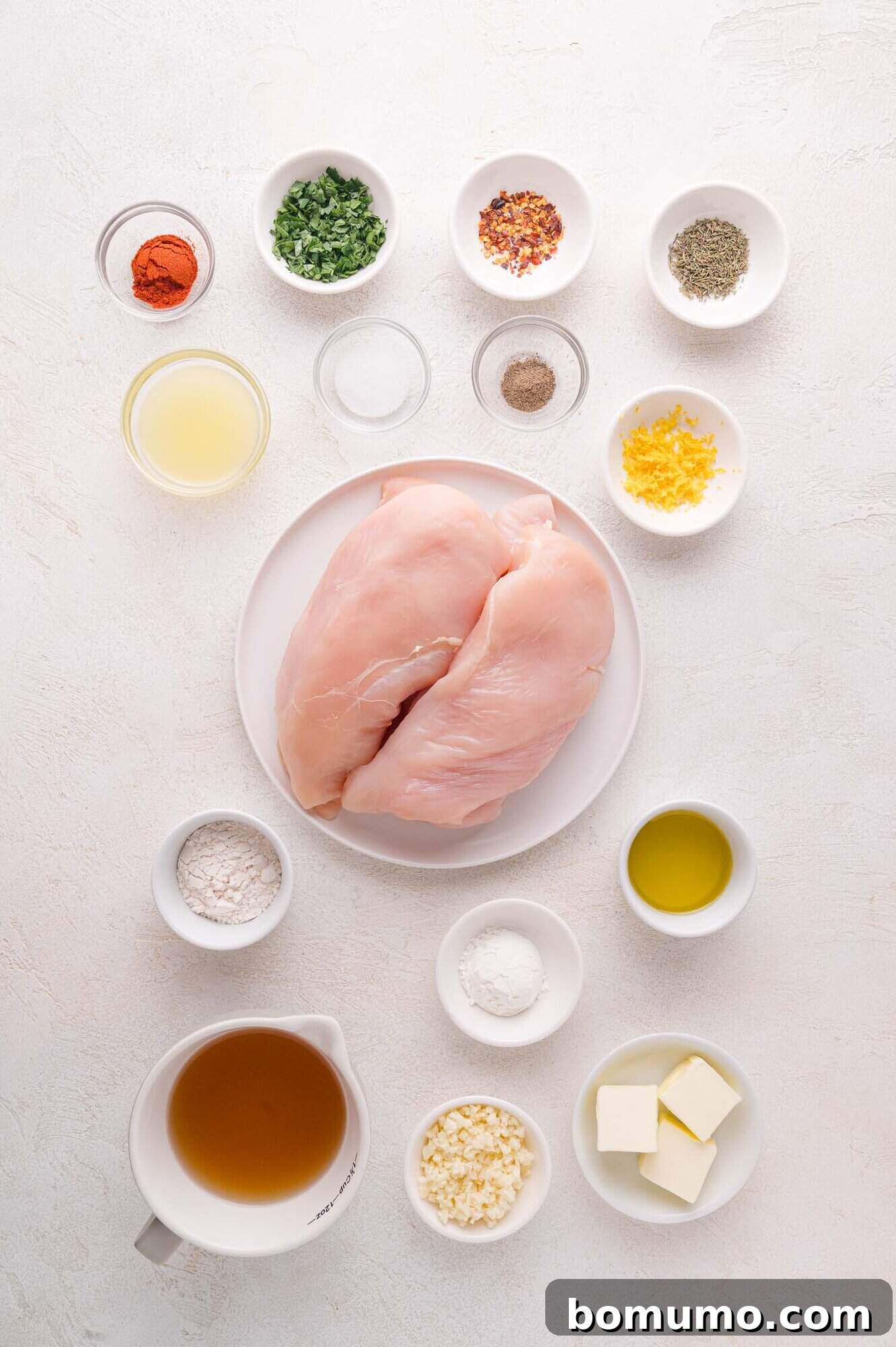 A meticulously arranged plate showcasing two raw chicken breasts, surrounded by an array of small, distinct bowls filled with various spices, fresh herbs, vibrant lemon zest, all-purpose flour, rich chicken broth, minced garlic, creamy butter, and golden olive oil on a clean white surface, highlighting the fresh ingredients ready for the Lemon Butter Chicken preparation.