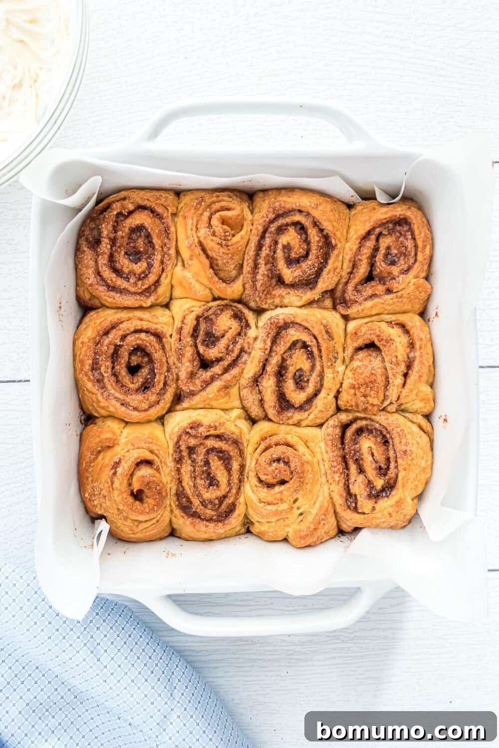 Quick Cinnamon Crescent Swirls 12 A white baking dish lined with parchment paper holds twelve freshly baked cinnamon rolls arranged in a 3x4 grid, golden brown and puffed.