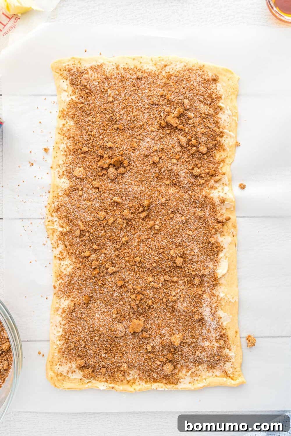Quick Cinnamon Crescent Swirls 7 A rectangular sheet of crescent dough covered with an even layer of cinnamon sugar mixture on a sheet of parchment paper, ready for rolling.