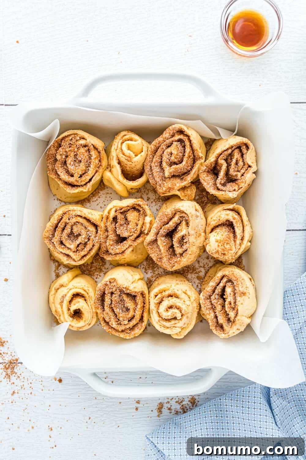 Quick Cinnamon Crescent Swirls 10 A square baking dish lined with parchment paper holds twelve unbaked cinnamon rolls arranged in a 3x4 grid, ready to be baked.