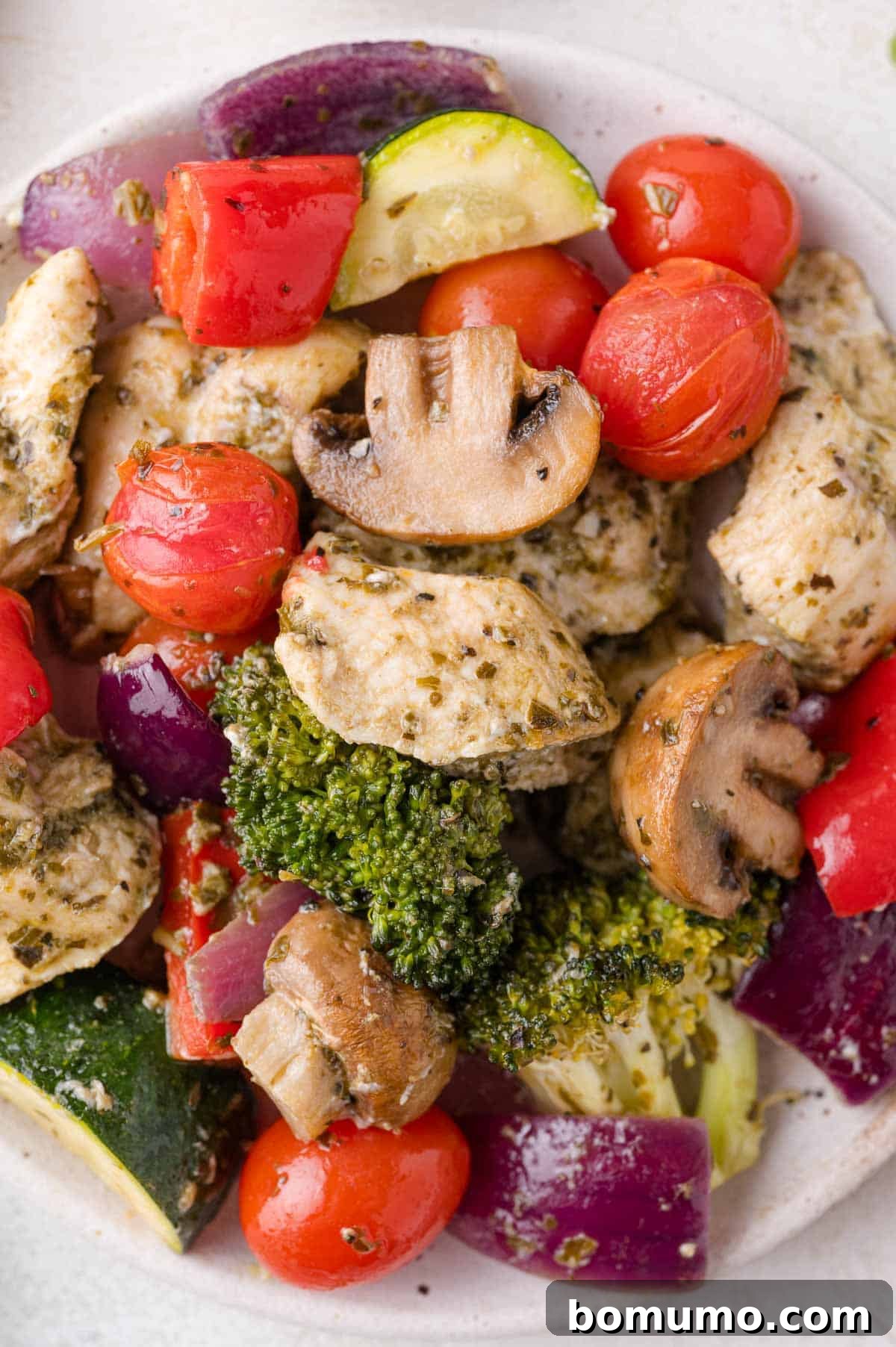 A perfectly plated serving of the delicious sheet pan pesto chicken, showcasing tender chicken cubes alongside a colorful array of roasted vegetables on a white dinner plate, ready to be enjoyed.