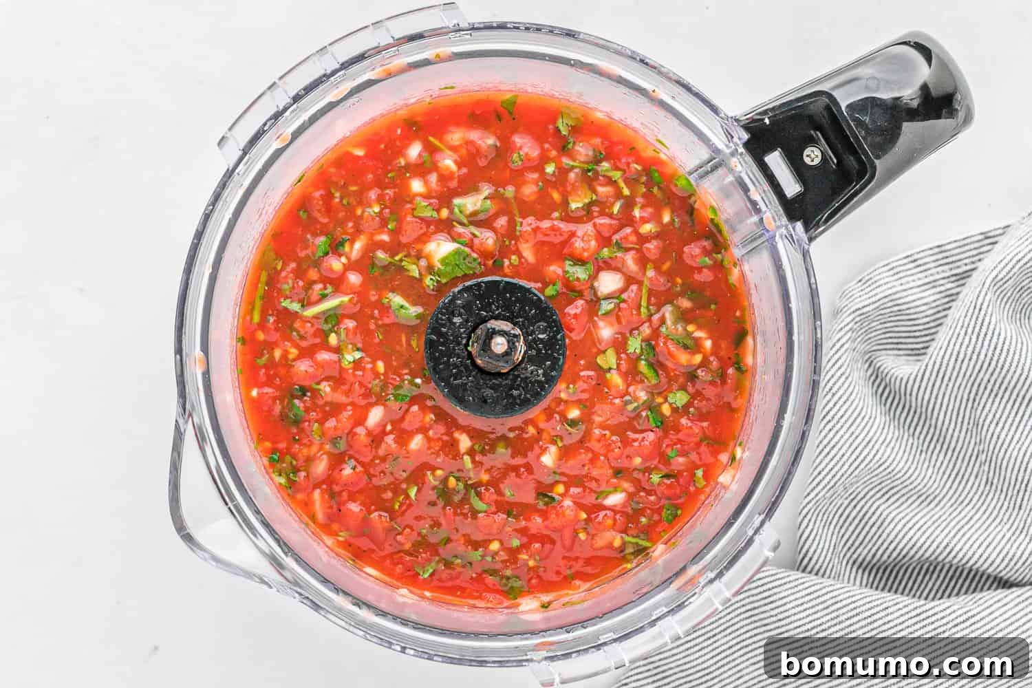 Freshly blended restaurant style salsa inside a food processor with a black handle, showcasing its chunky texture.