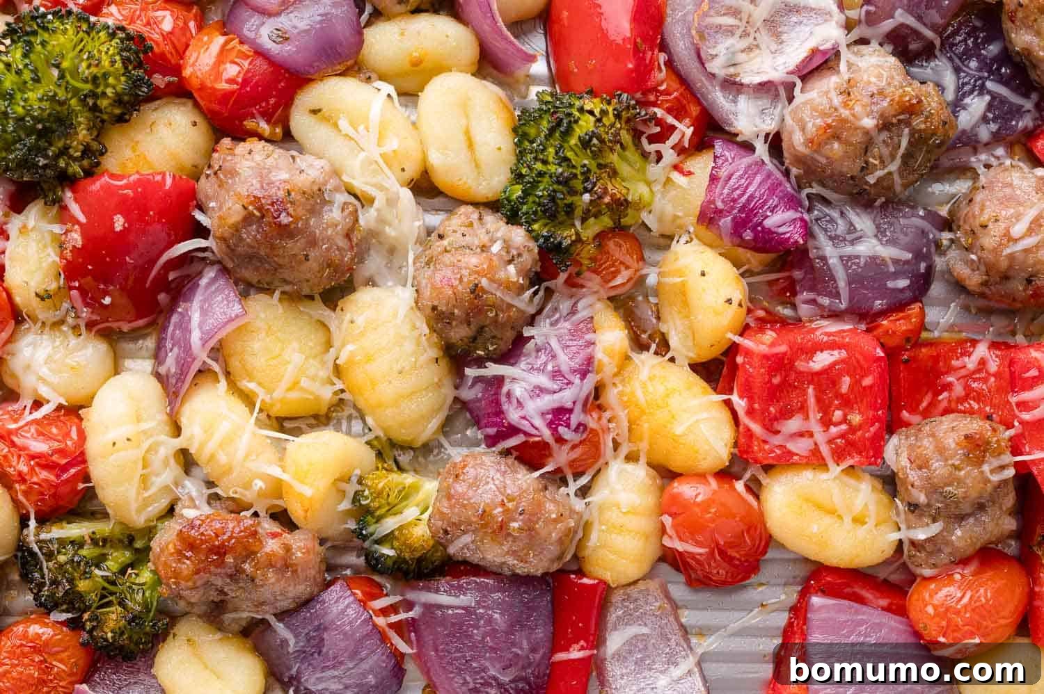 A large sheet pan brimming with perfectly cooked gnocchi, crumbled Italian sausage, vibrant red onion, crisp broccoli florets, sweet red bell pepper, juicy cherry tomatoes, all generously topped with melted shredded cheese.
