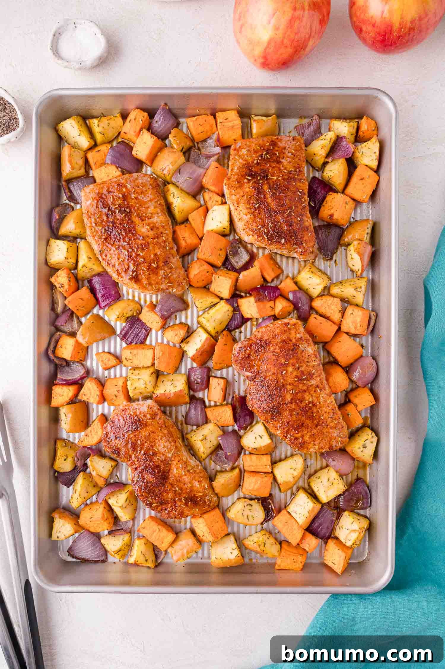 A beautifully baked sheet pan dinner featuring golden-brown pork chops surrounded by perfectly roasted sweet potatoes, caramelized apples, and tender red onions, arranged on the pan and ready to be served.