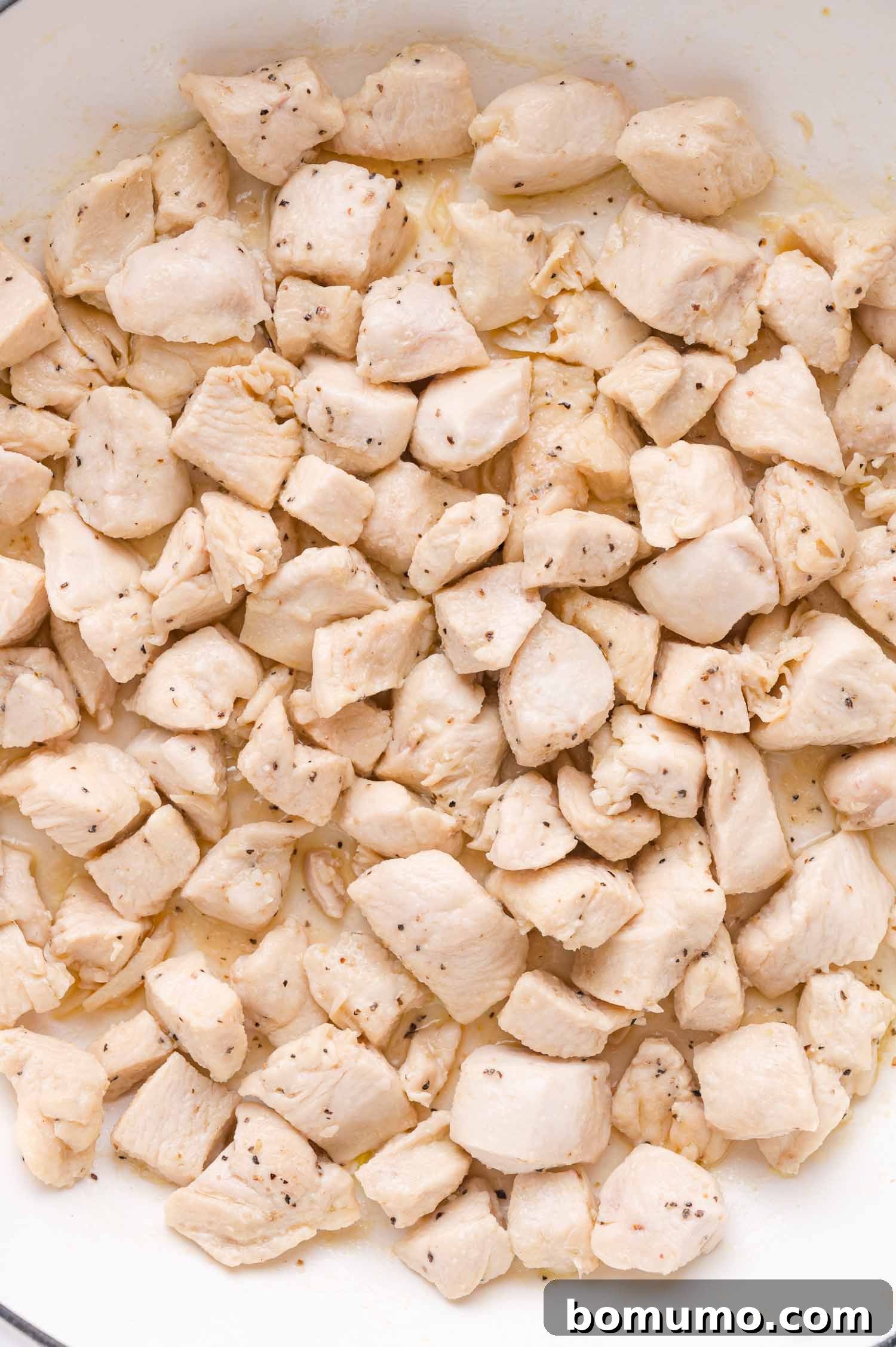 A close-up, top-down view of tender, diced chicken breast pieces, perfectly seasoned with salt and freshly ground black pepper, glistening in a pan.
