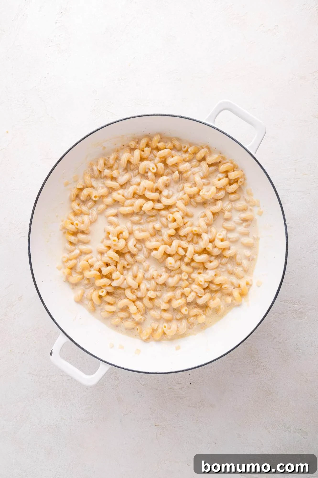 A white pot on a light surface, brimming with perfectly cooked cavatappi pasta coated in a luxurious, creamy liquid, ready for the next step.