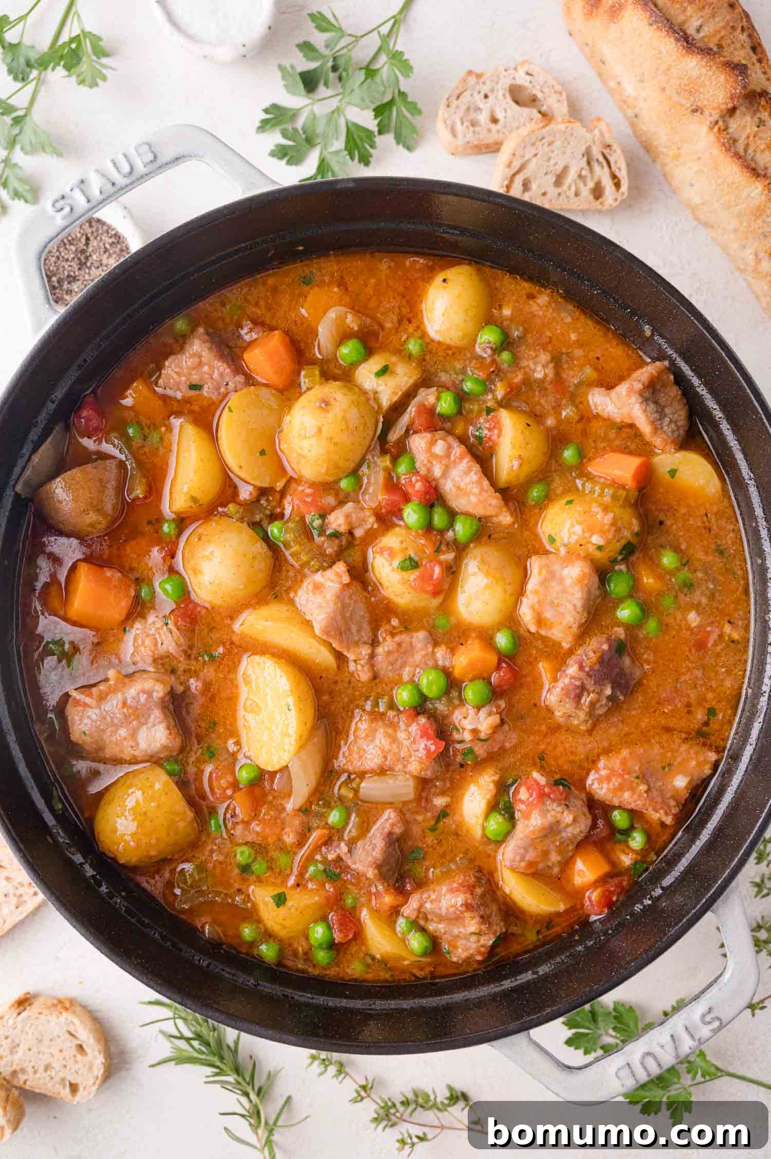 Tender Pork Ragout 2 A pot of hearty pork stew with succulent chunks of pork, tender potatoes, vibrant carrots, sweet peas, and a rich, tomato-infused broth, perfectly complemented by crusty bread and fresh herbs.