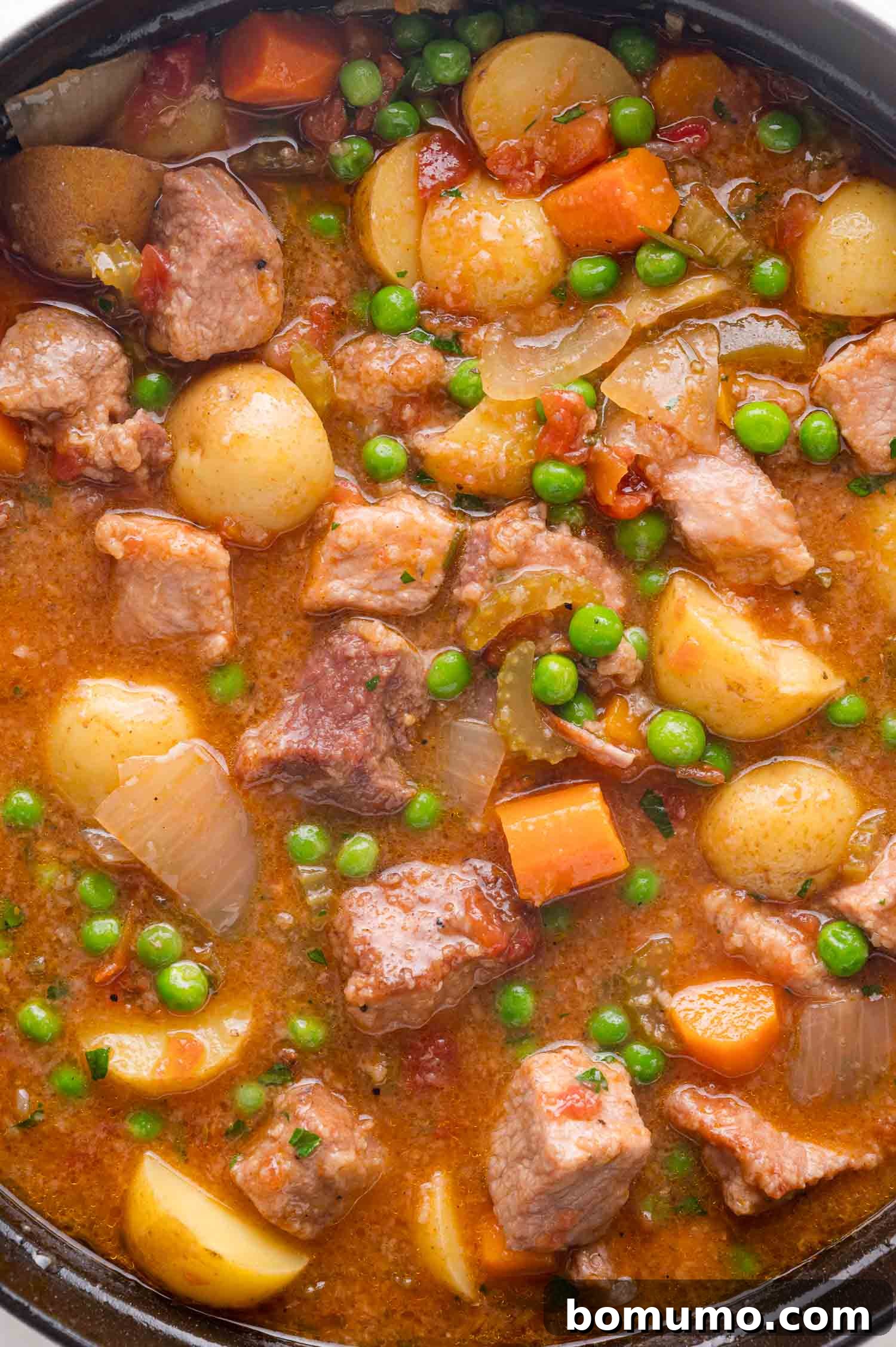 Tender Pork Ragout 18 A close-up of a pot filled with perfectly cooked pork stew, showcasing tender chunks of pork, soft potatoes, vibrant carrots, green peas, and onions in a rich, flavorful broth.
