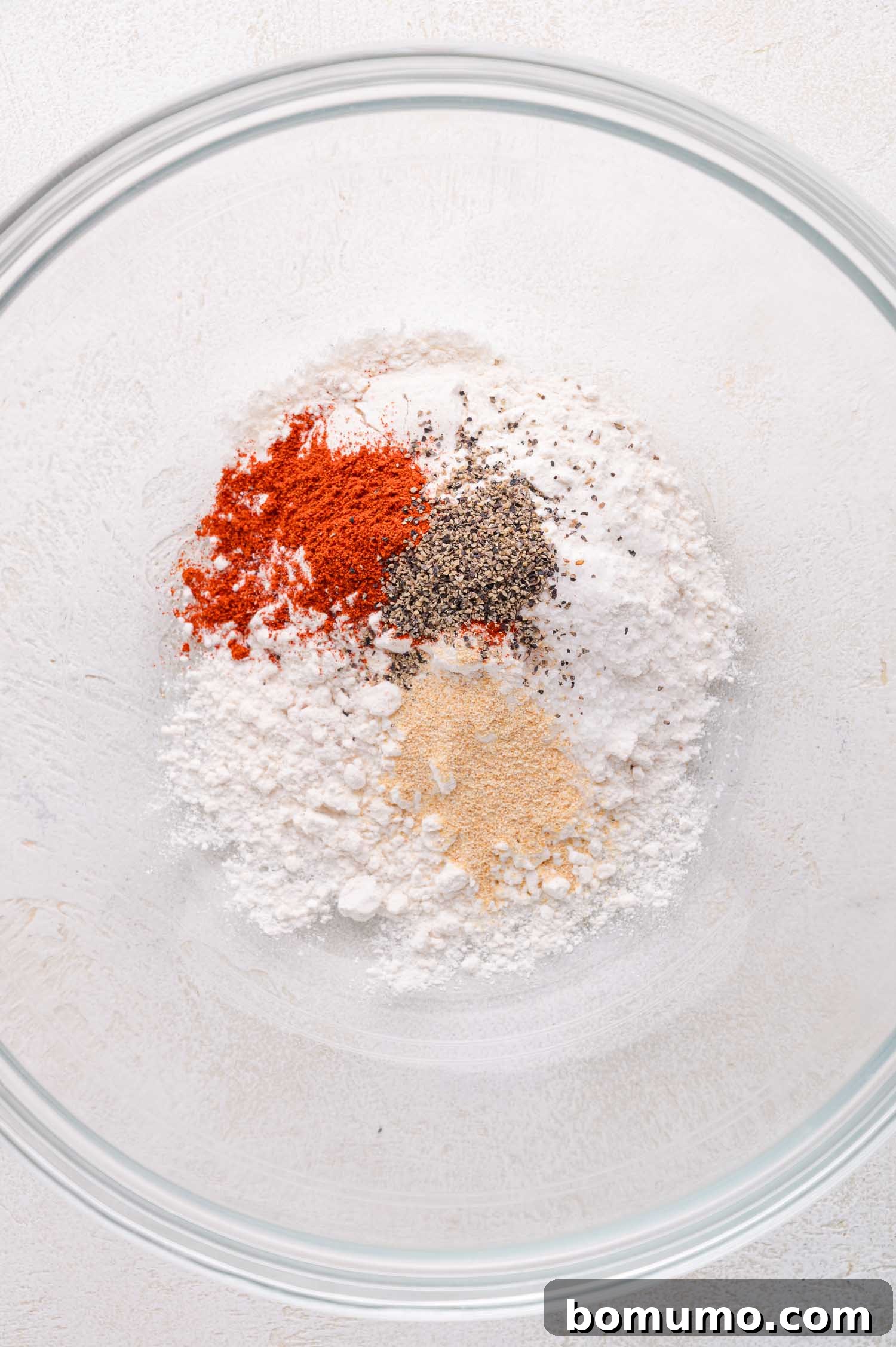 Tender Pork Ragout 5 Clear glass bowl containing separate piles of white flour, paprika, black pepper, garlic powder, and salt on a light surface, illustrating the spice blend.