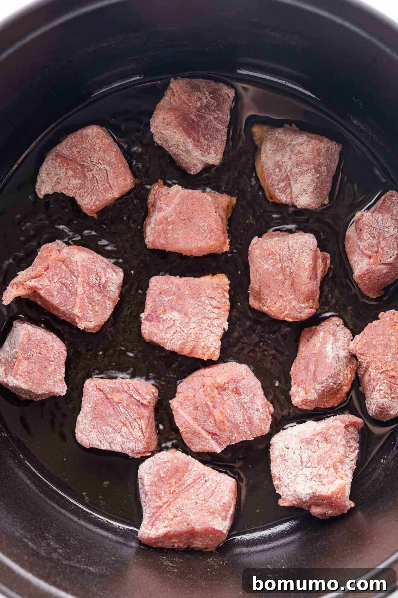 Tender Pork Ragout 7 Raw beef cubes arranged in a single layer inside a black pot with a small amount of oil at the bottom, ready for searing.