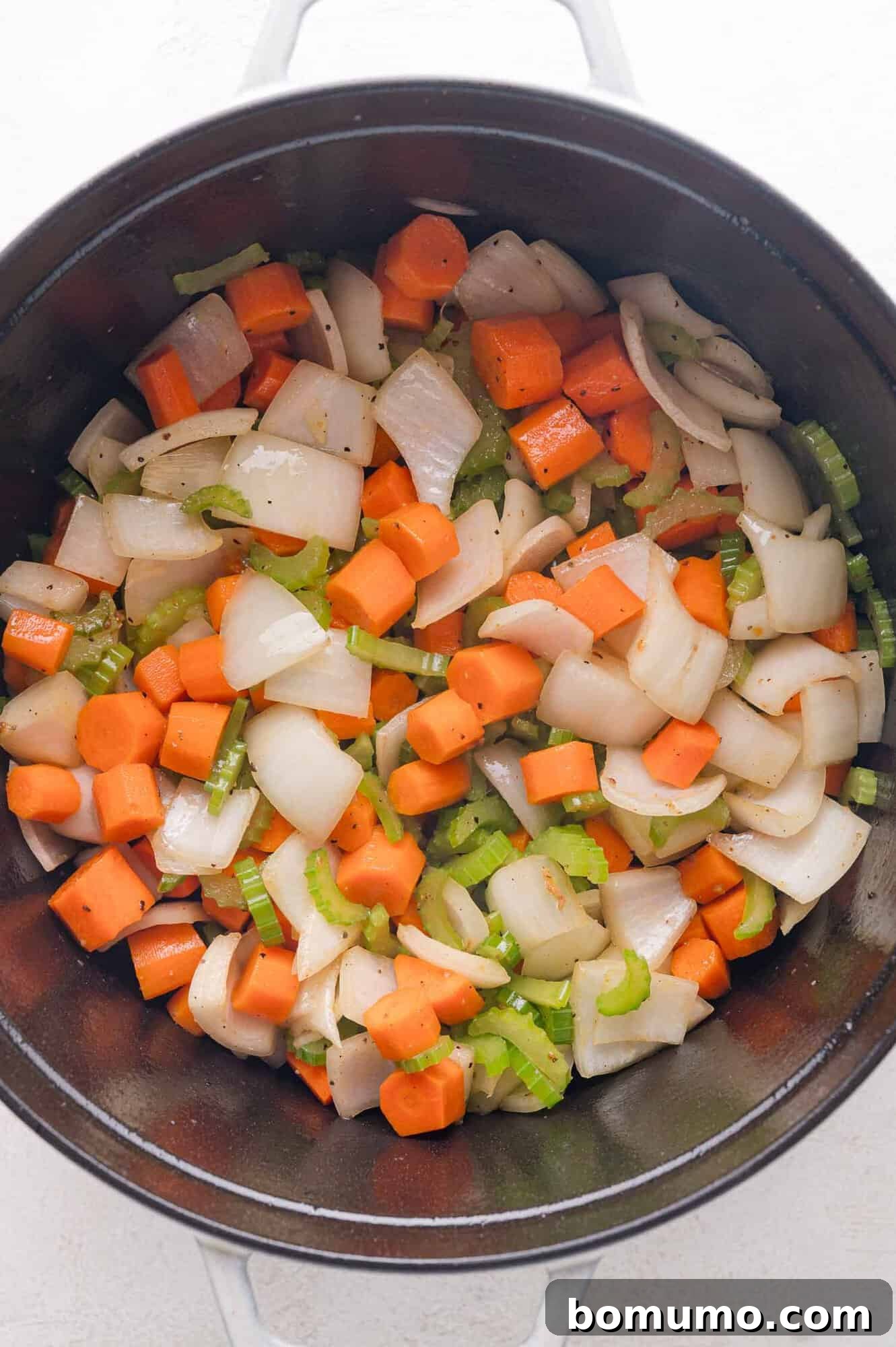 Tender Pork Ragout 9 Chopped carrots, celery, and onions sautéing in a black pot, forming the aromatic base of the stew.