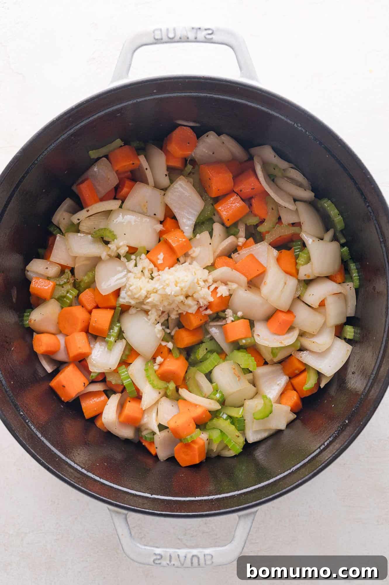 Tender Pork Ragout 10 Chopped onions, carrots, and celery with minced garlic in a large black pot, viewed from above, showcasing the fragrant aromatics.