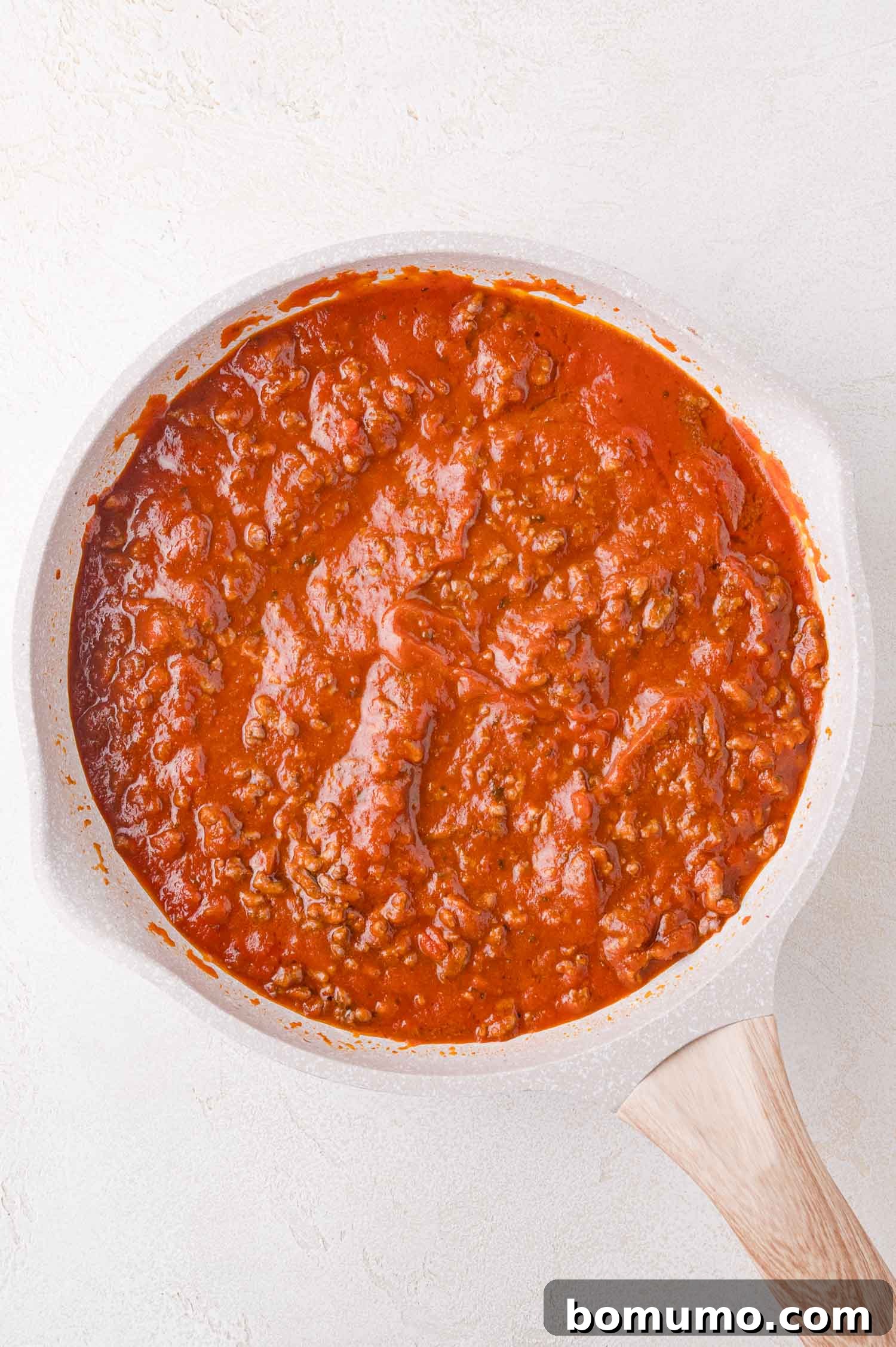 A pristine white pan holds a generous quantity of classic meat sauce, a perfect blend of rich tomato and savory ground meat, gleaming invitingly on a light-colored kitchen counter.