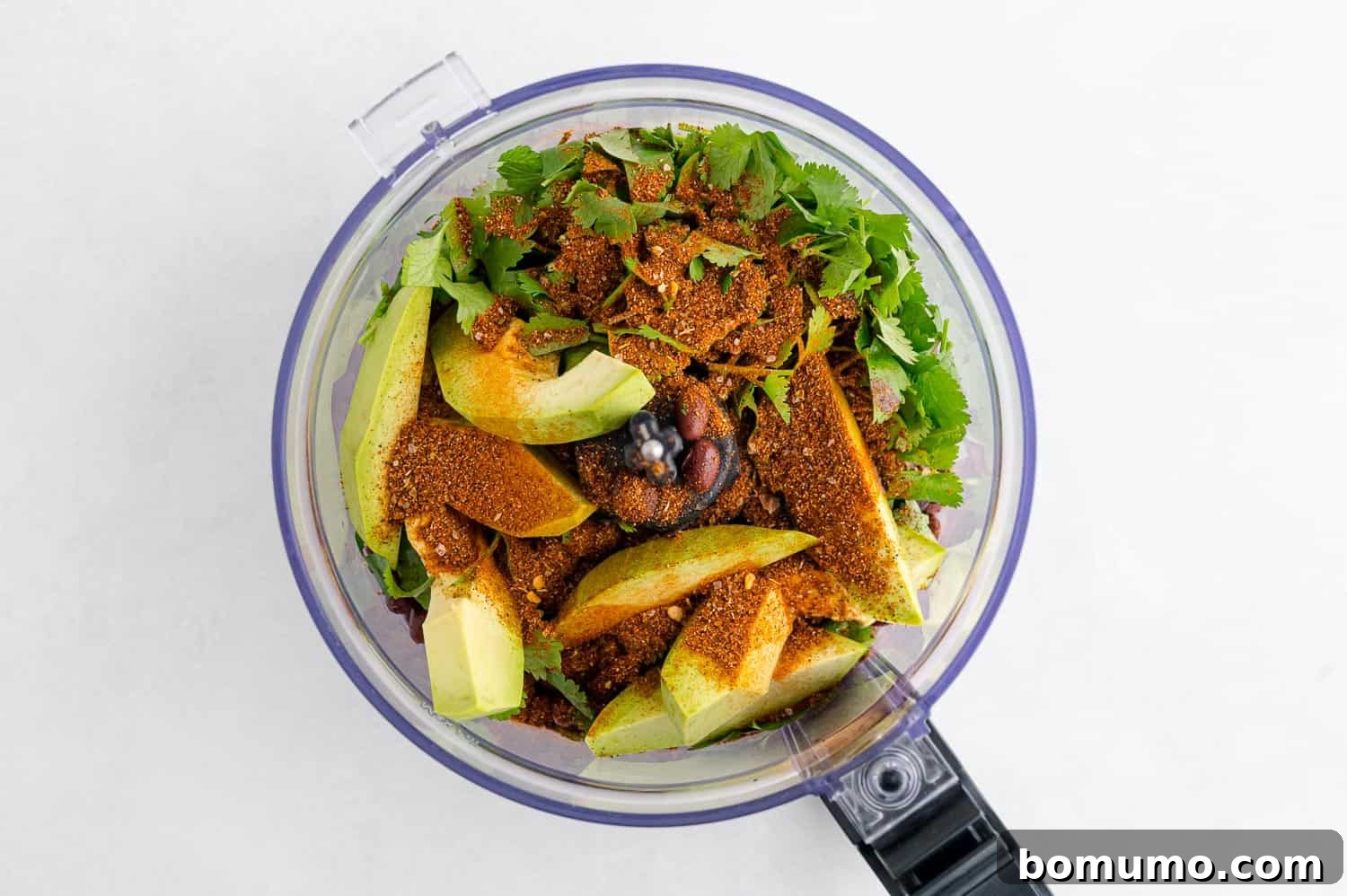 All ingredients for black bean dip, including beans, seasoning, and avocado, placed in a food processor, ready for blending.
