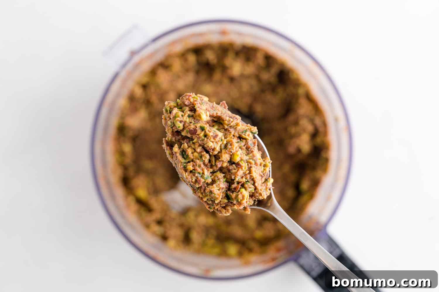 A spatula scooping creamy black bean dip from a food processor into a serving bowl, ready for chilling.